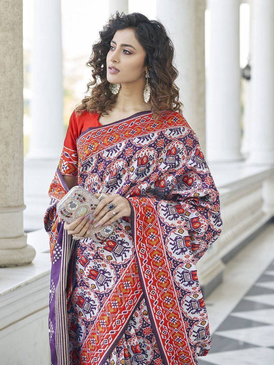 Woman in vibrant printed saree with red blouse, ethnic jewelry, and embellished clutch, perfect for Indian festive occasions