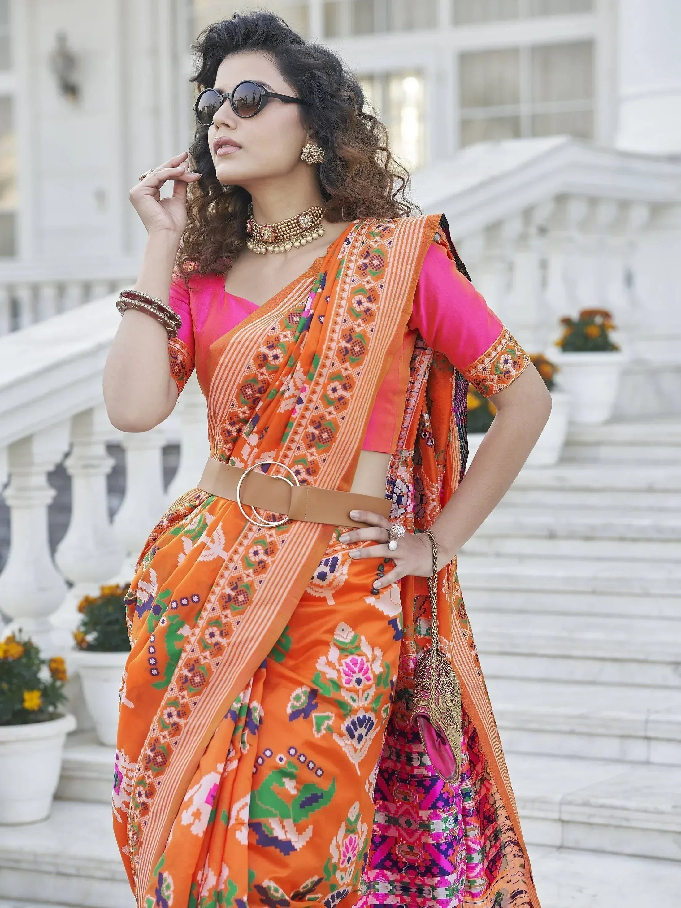 Vibrant orange printed saree with pink blouse, styled with belt and traditional jewelry for ethnic wear