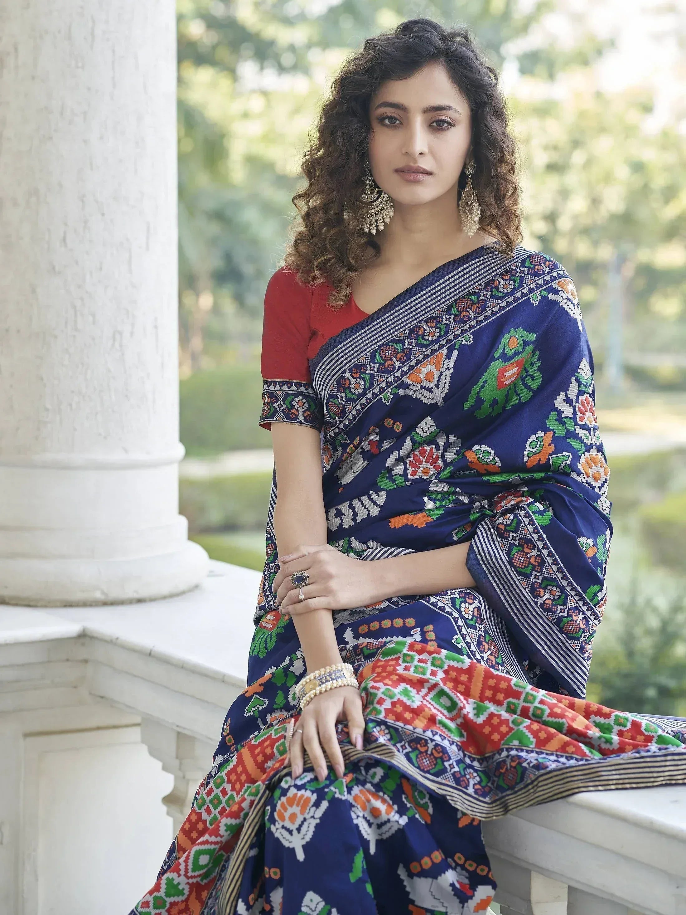 Woman in vibrant blue printed saree with red blouse, ethnic jewelry, and floral patterns