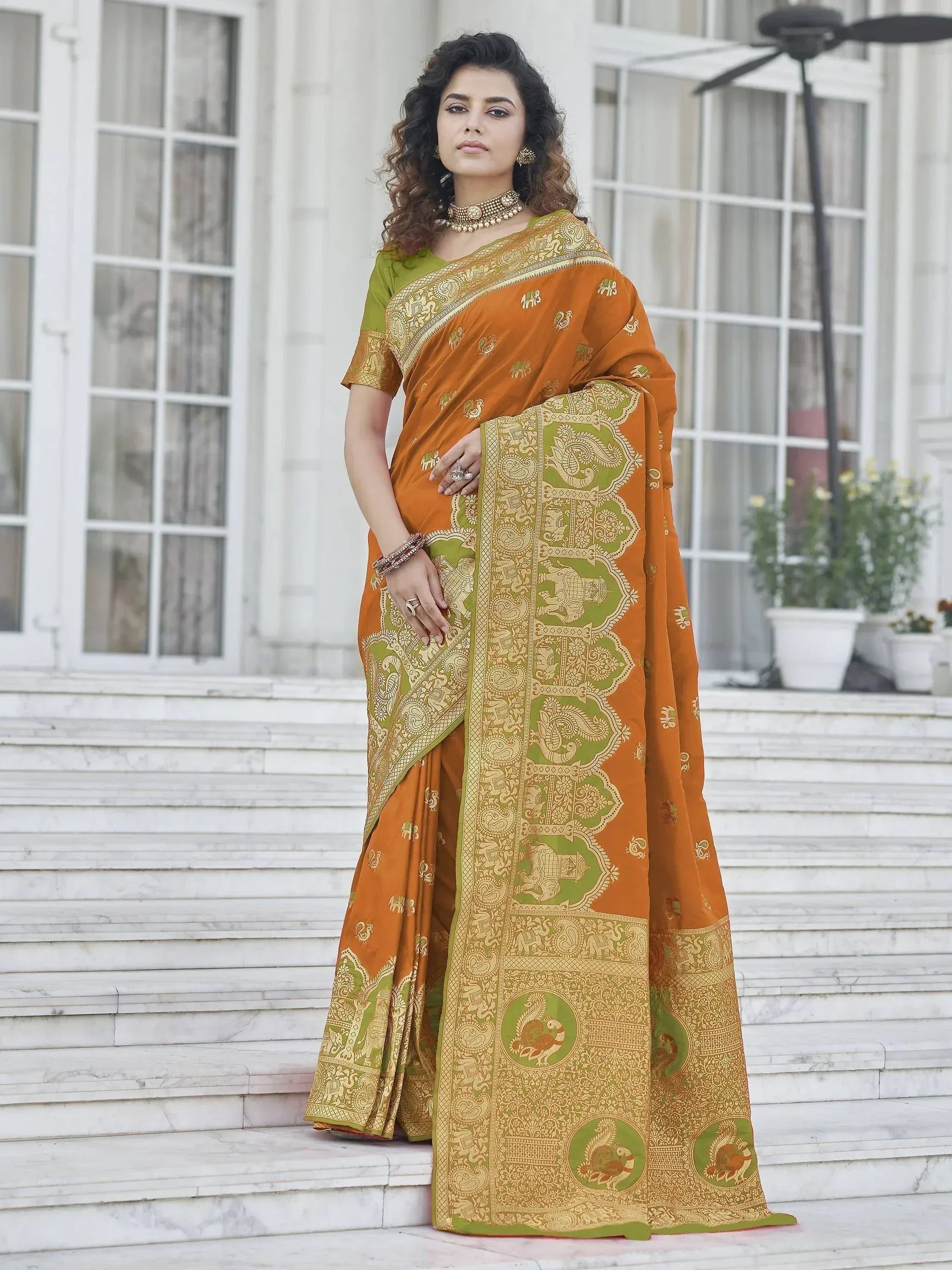 Woman in orange and green designer saree with elephant and peacock motifs, perfect for Indian ethnic occasions