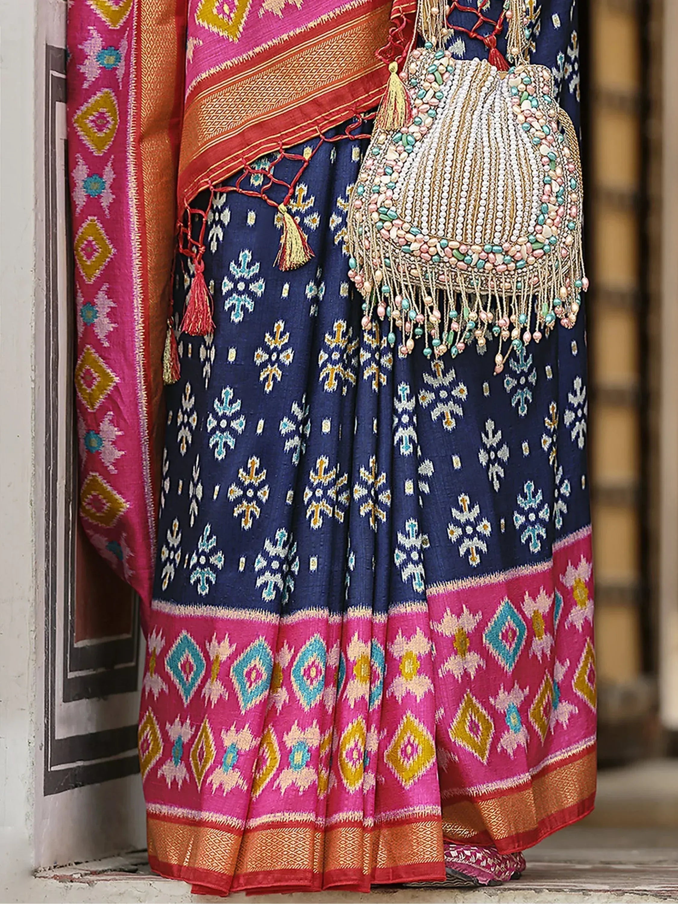 Blue and pink ethnic saree with intricate ikat patterns and beaded potli bag, perfect for Indian celebrations
