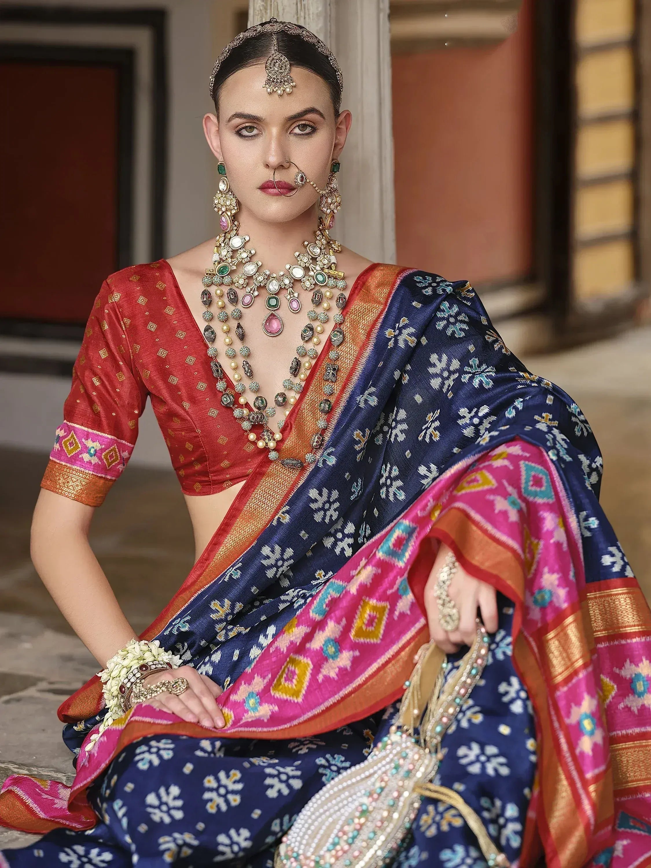 Woman in vibrant blue and pink ethnic saree with red blouse, traditional jewelry, and floral patterns