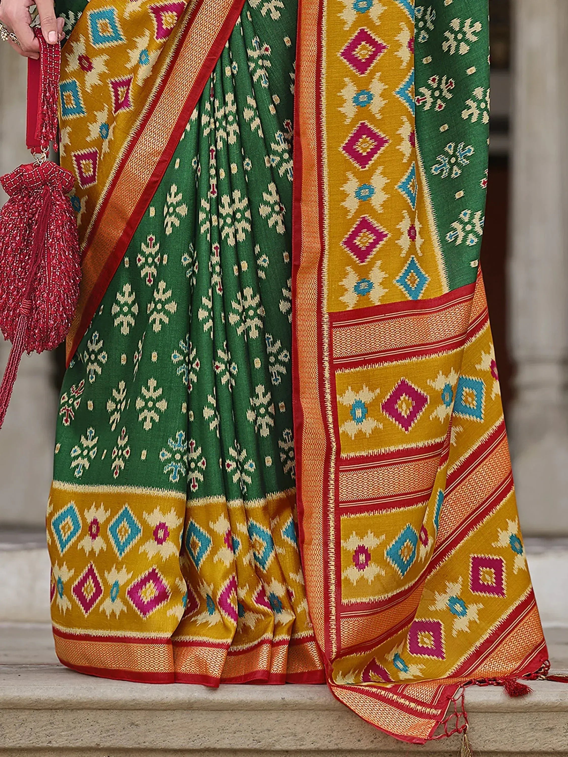 Green and mustard Indian saree with geometric ikat print, red border, and matching potli bag