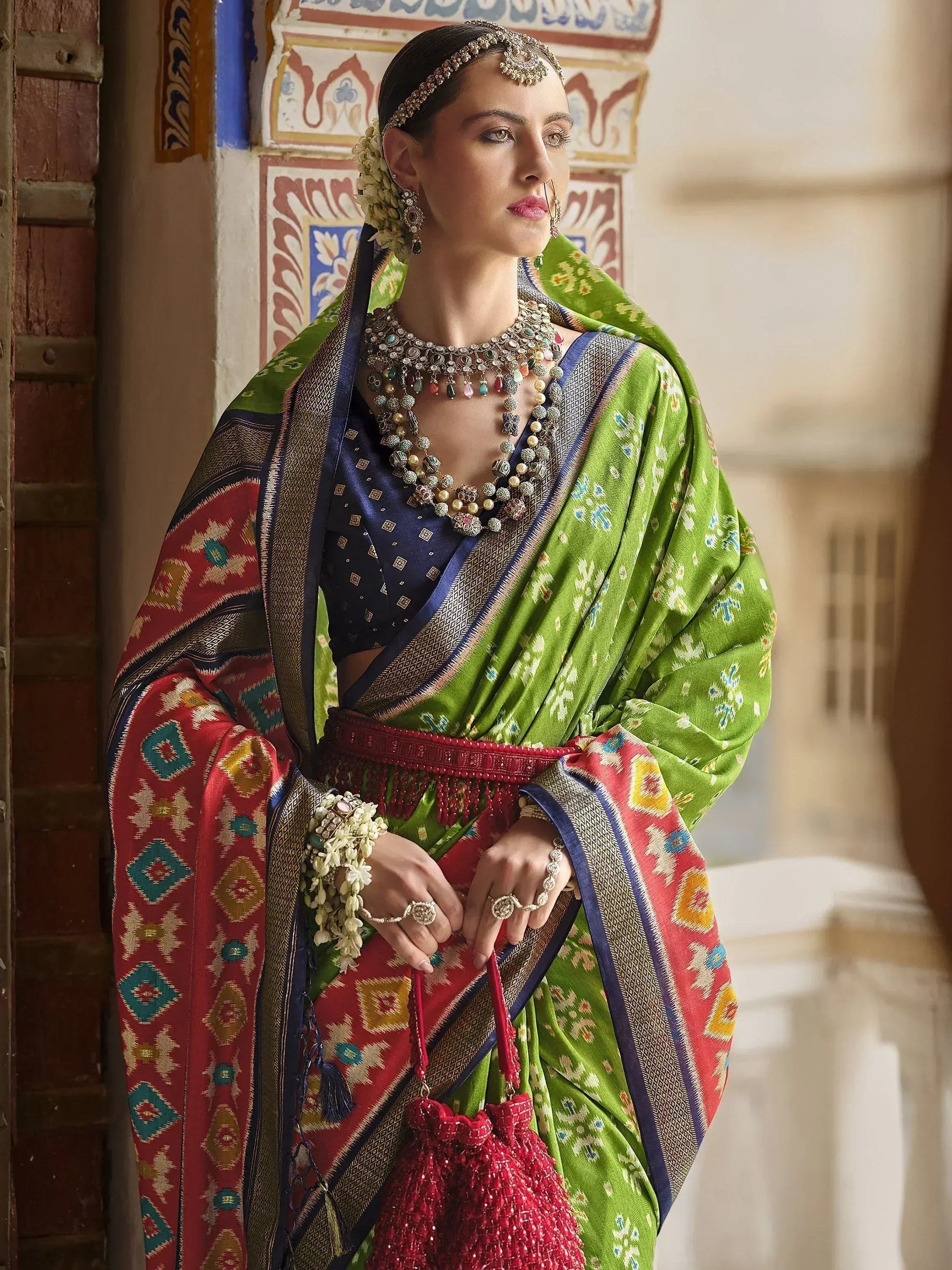 Woman in vibrant green and red ethnic saree with intricate jewelry and floral accessories