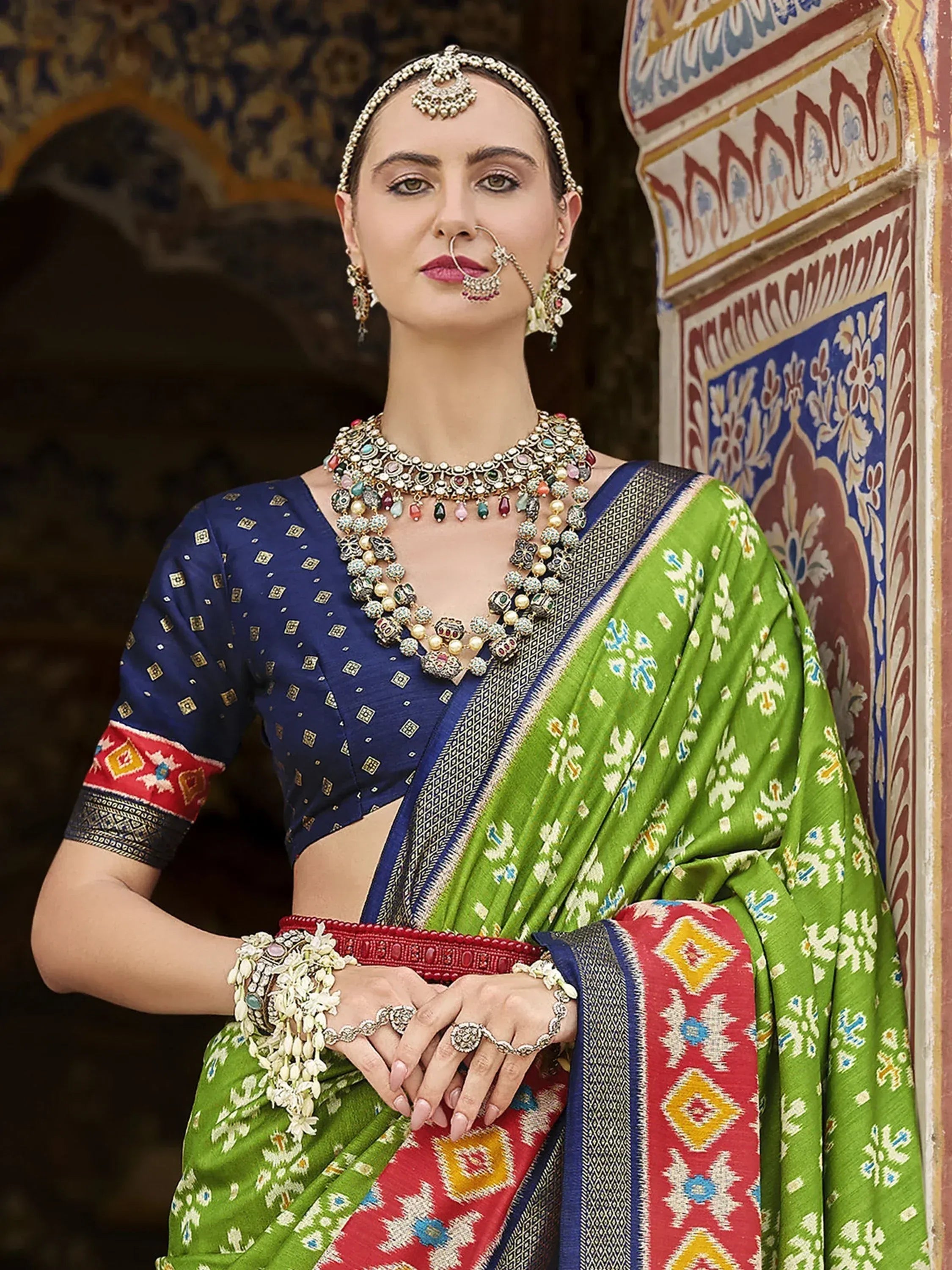 Woman in vibrant green and blue ethnic saree with intricate jewelry, traditional Indian attire
