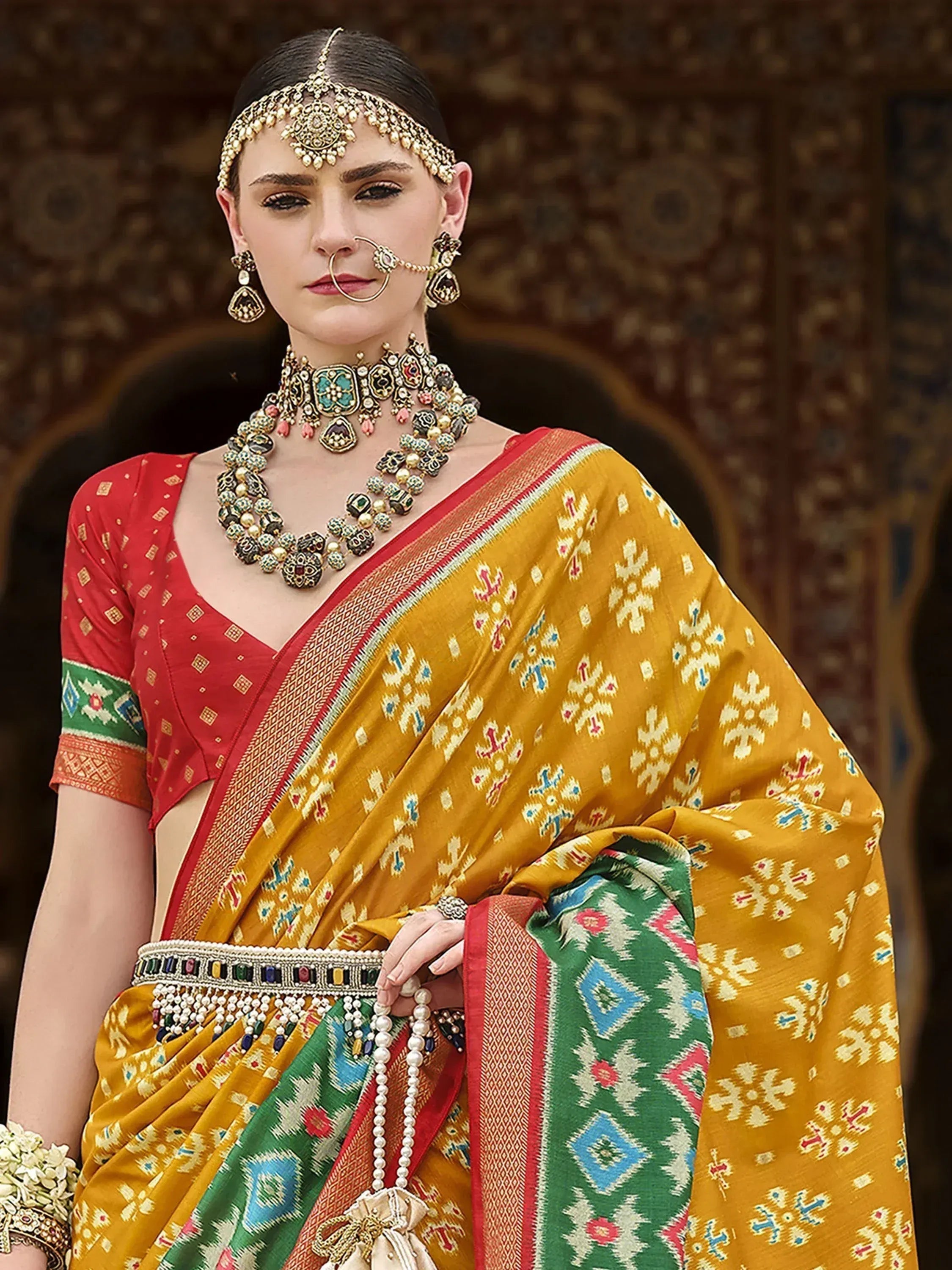 Woman in vibrant yellow ikat saree with red blouse, traditional Indian jewelry, and ornate temple backdrop