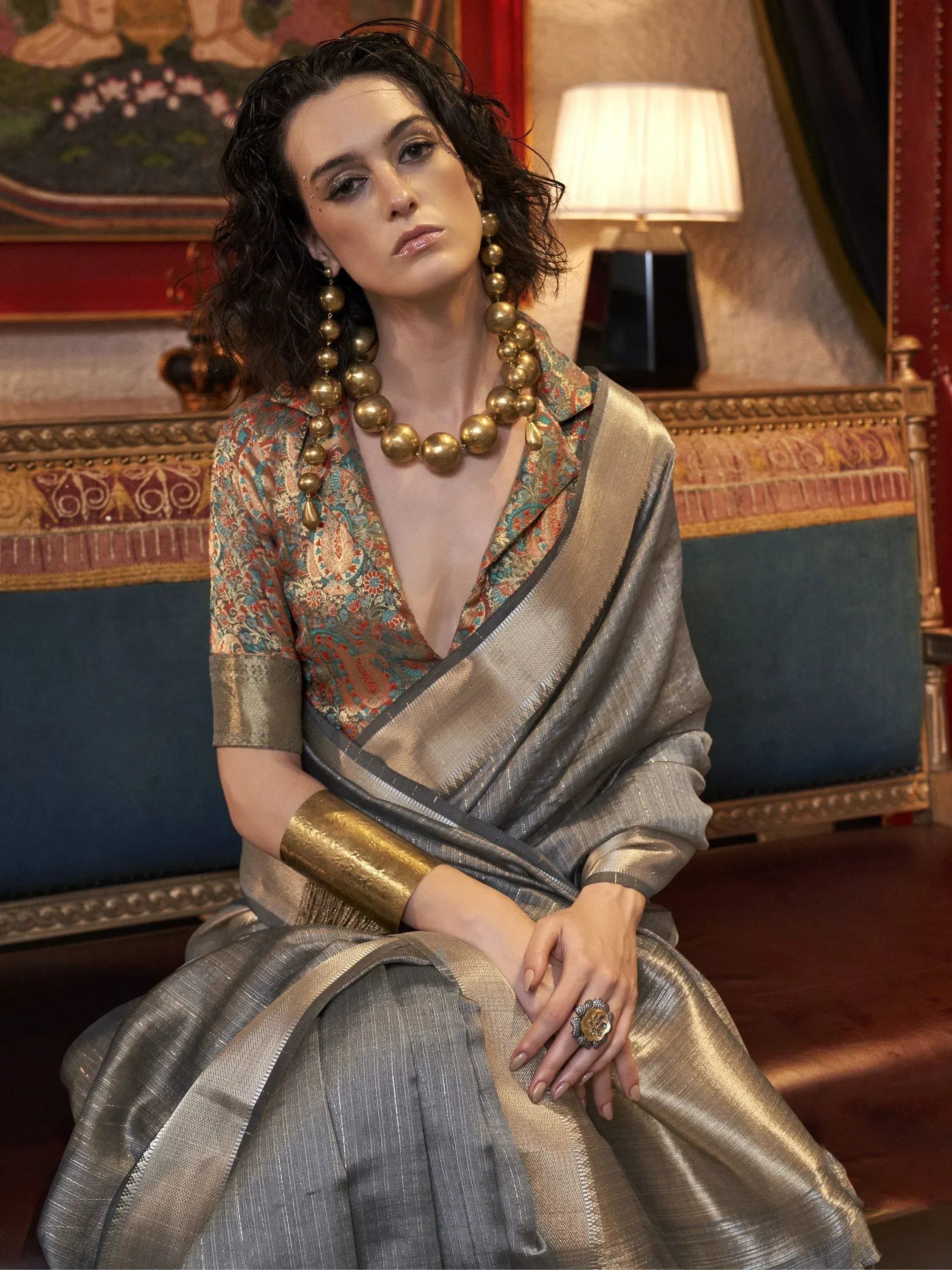 Woman in elegant Indian ethnic saree with gold jewelry, designer blouse, and statement accessories