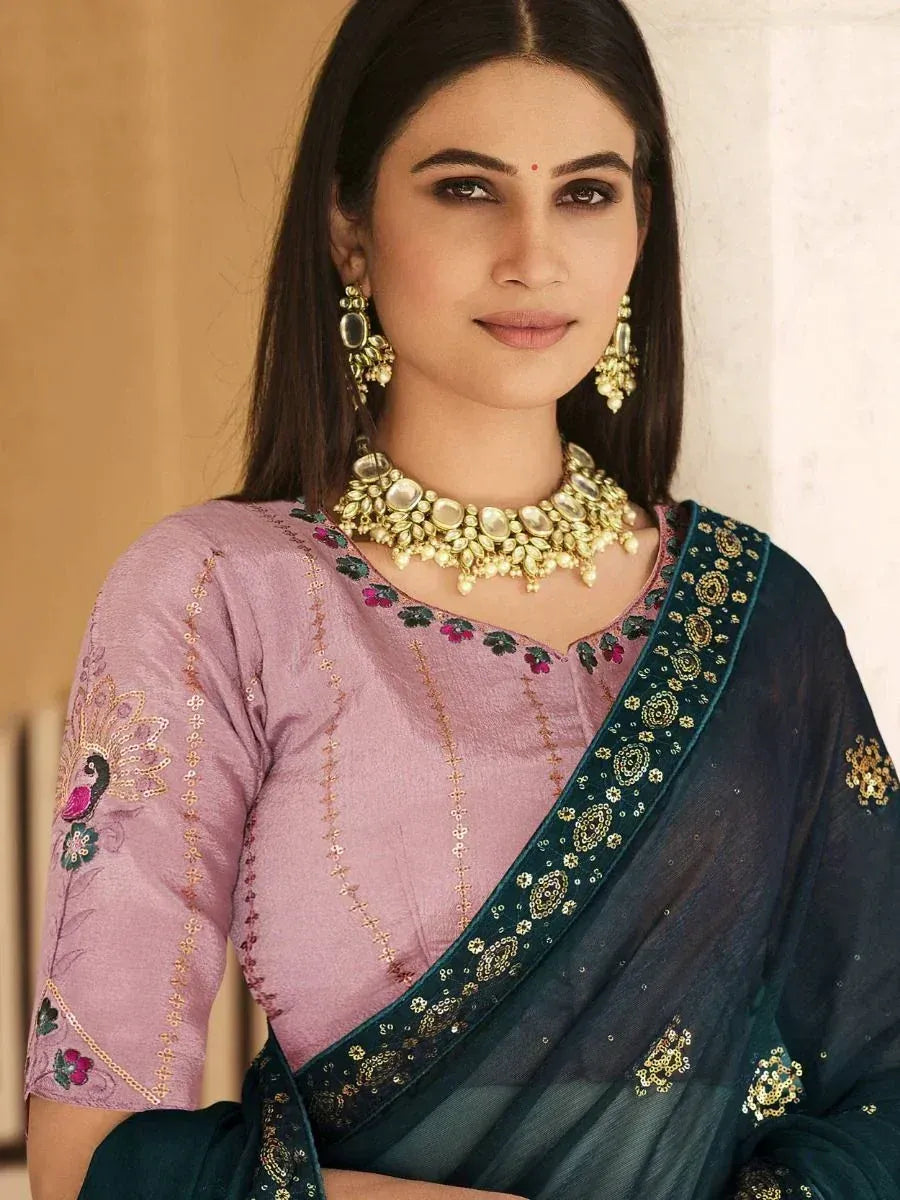 Elegant woman in pink embroidered blouse with peacock design, paired with dark green saree and gold jewelry, showcasing Indian ethnic wear.
