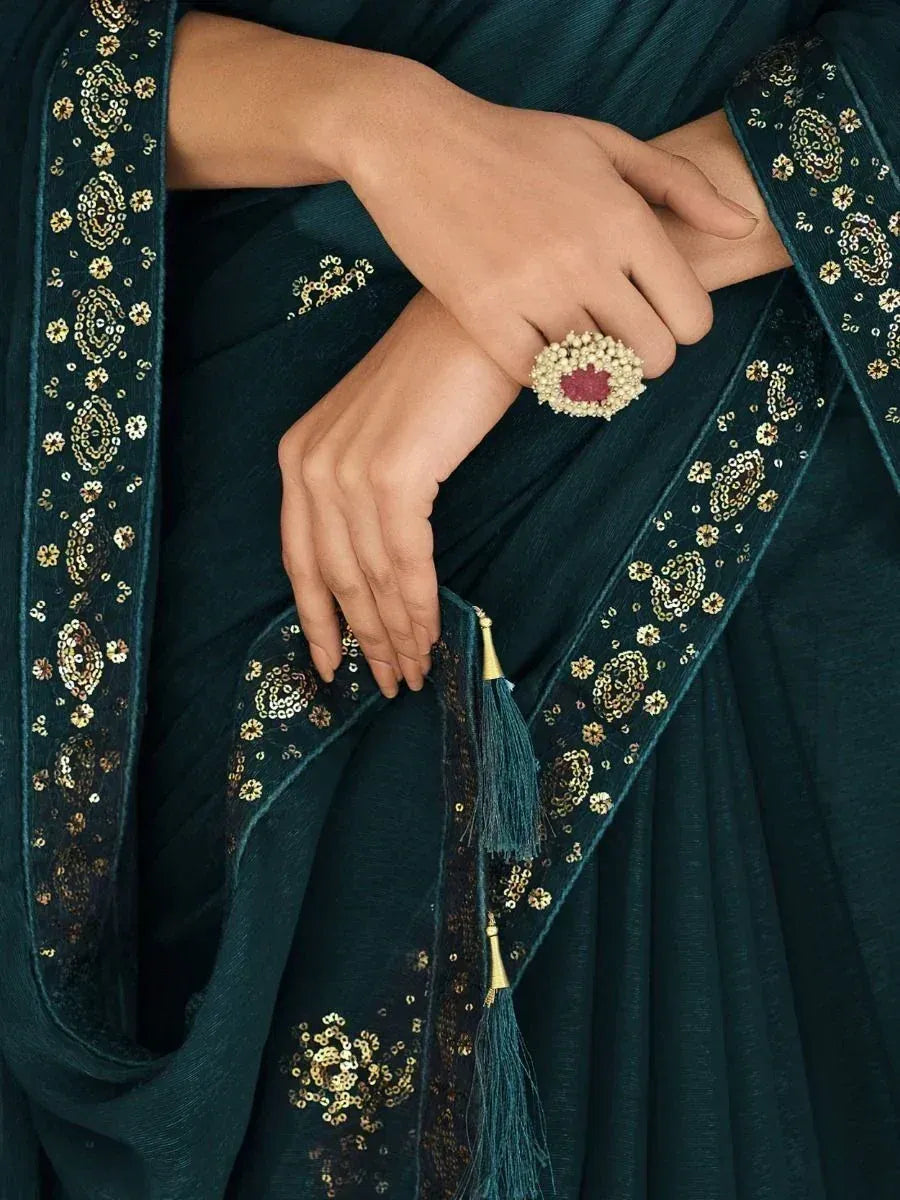 Elegant teal saree with gold embroidery and tassels, paired with a statement ring