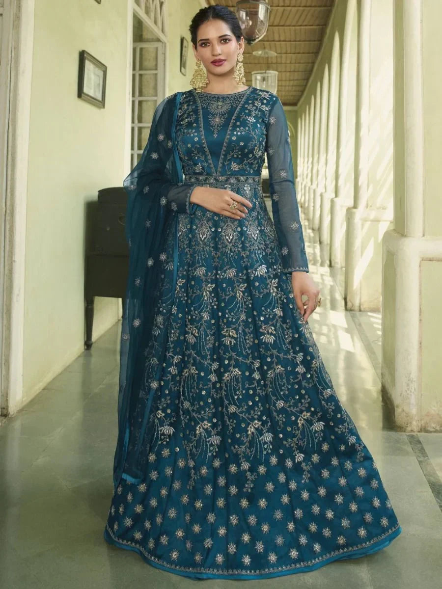 Woman in blue embroidered ethnic gown with net dupatta, standing in corridor
