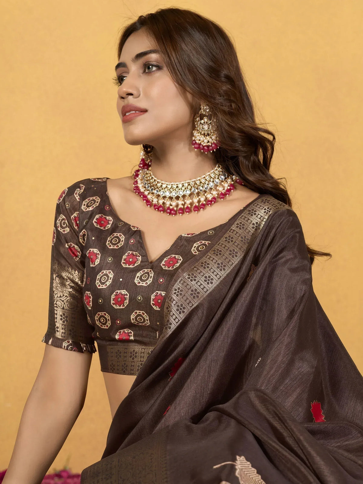 Brown printed saree with gold border and red floral motifs, paired with traditional jewelry for ethnic wear