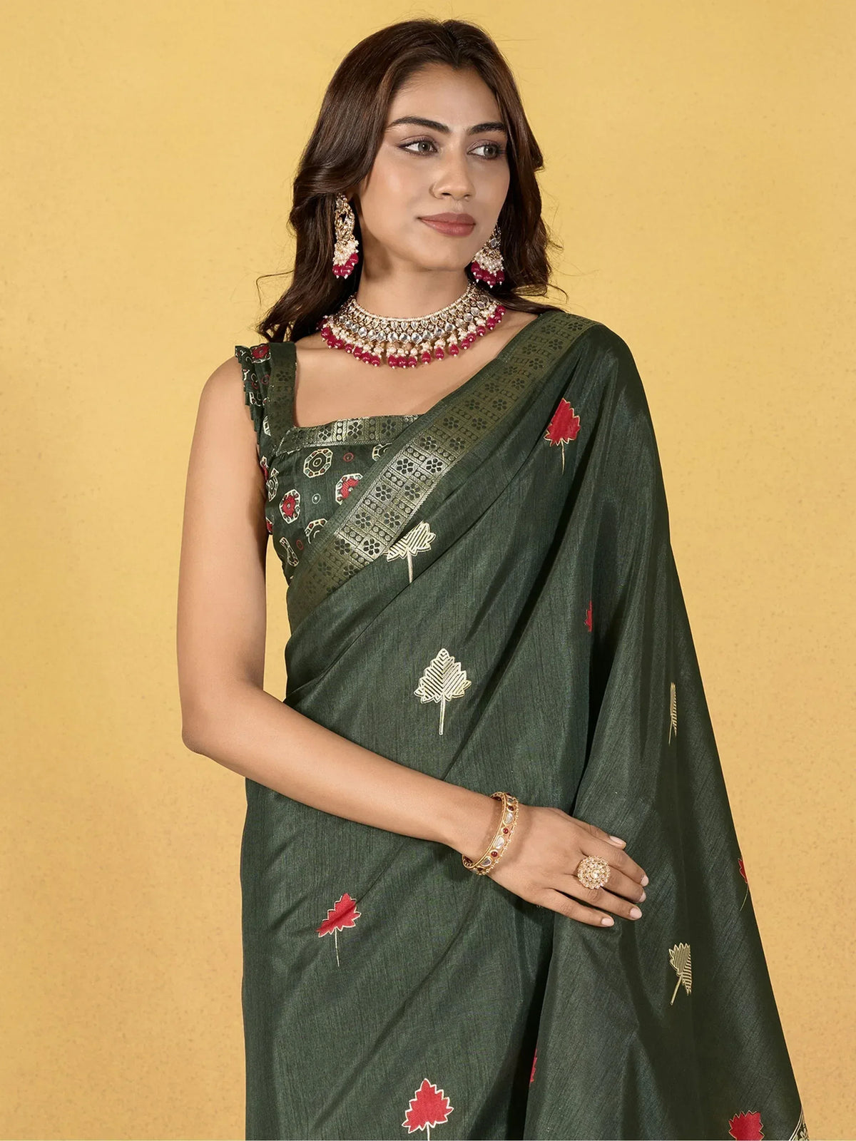 Woman in olive green embroidered saree with red and gold leaf motifs, paired with traditional jewelry.