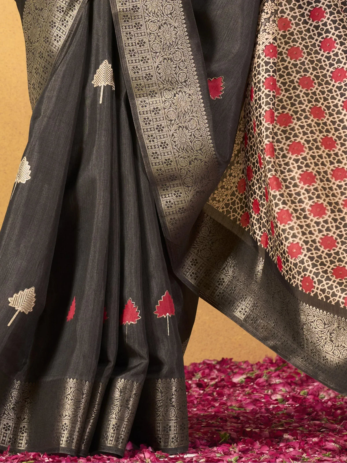 Black saree with gold zari border and red leaf motifs, ethnic Indian wear on rose petals