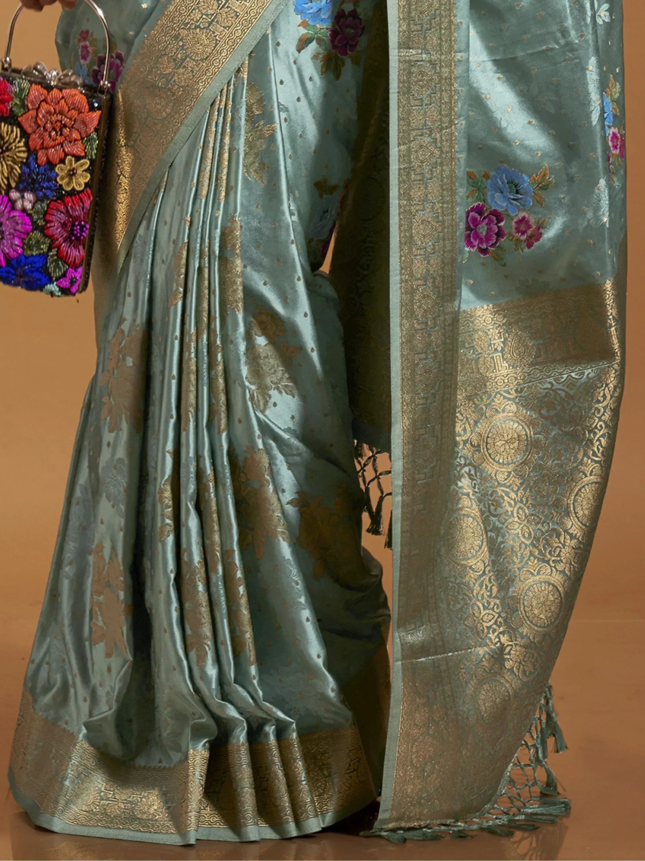 Elegant teal saree with gold floral embroidery and zari border, paired with colorful floral handbag
