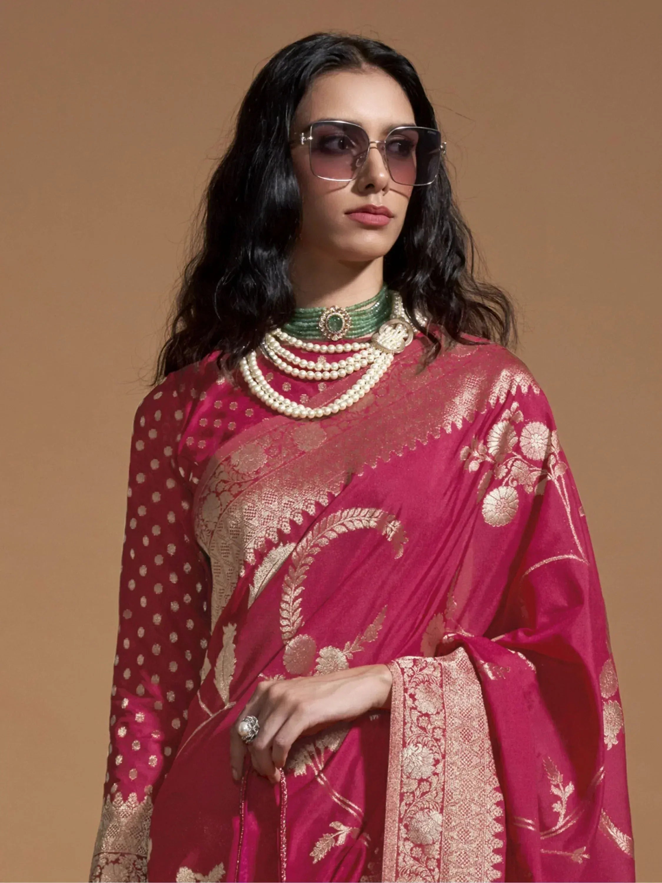 Woman in pink designer saree with gold embroidery, pearl jewelry, and sunglasses