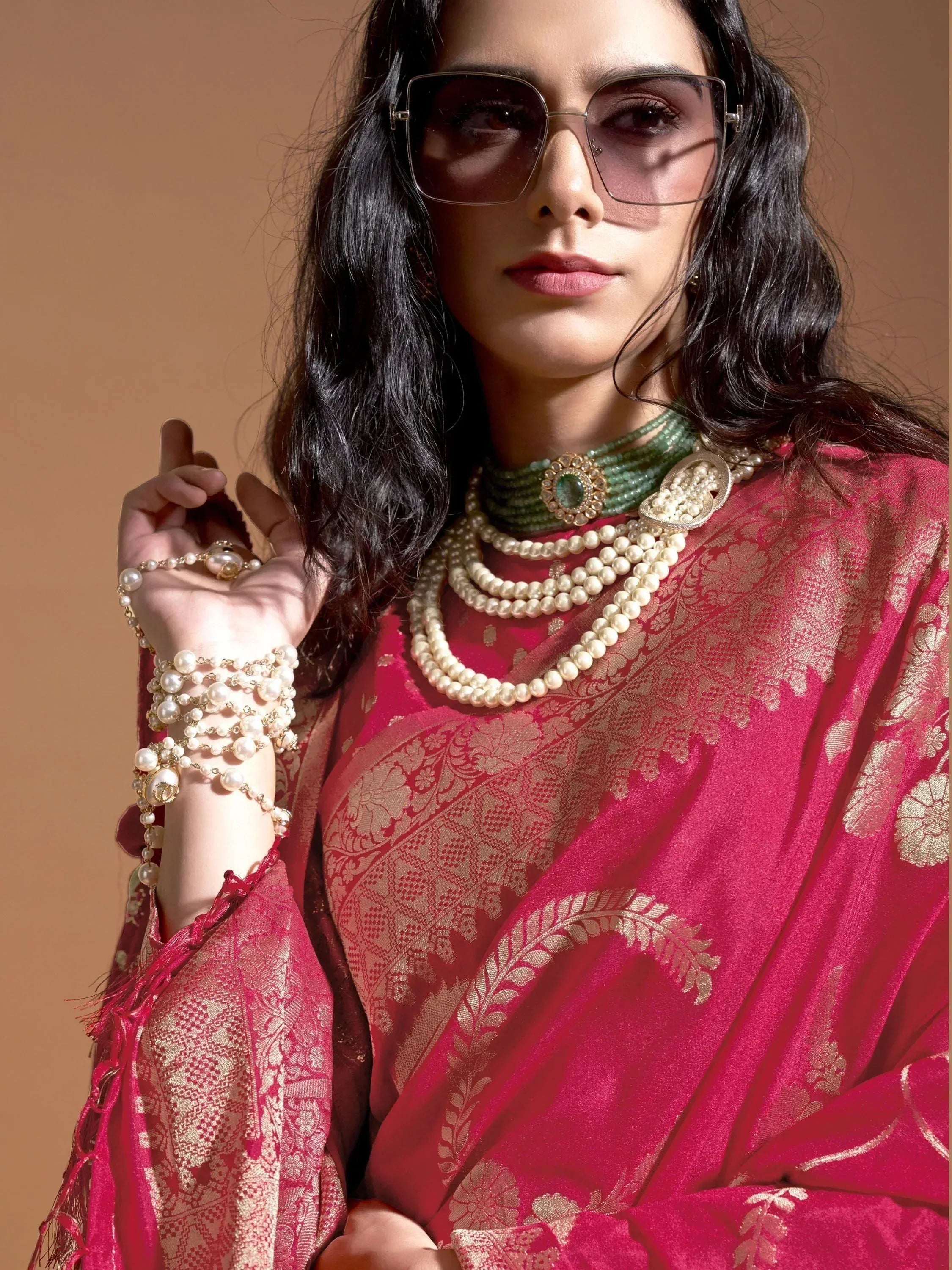 Woman in pink ethnic saree with gold embroidery, pearl jewelry, and sunglasses