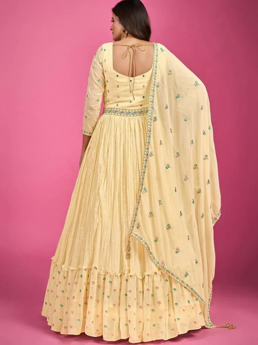 Woman wearing a pastel yellow embroidered lehenga choli with dupatta against pink background