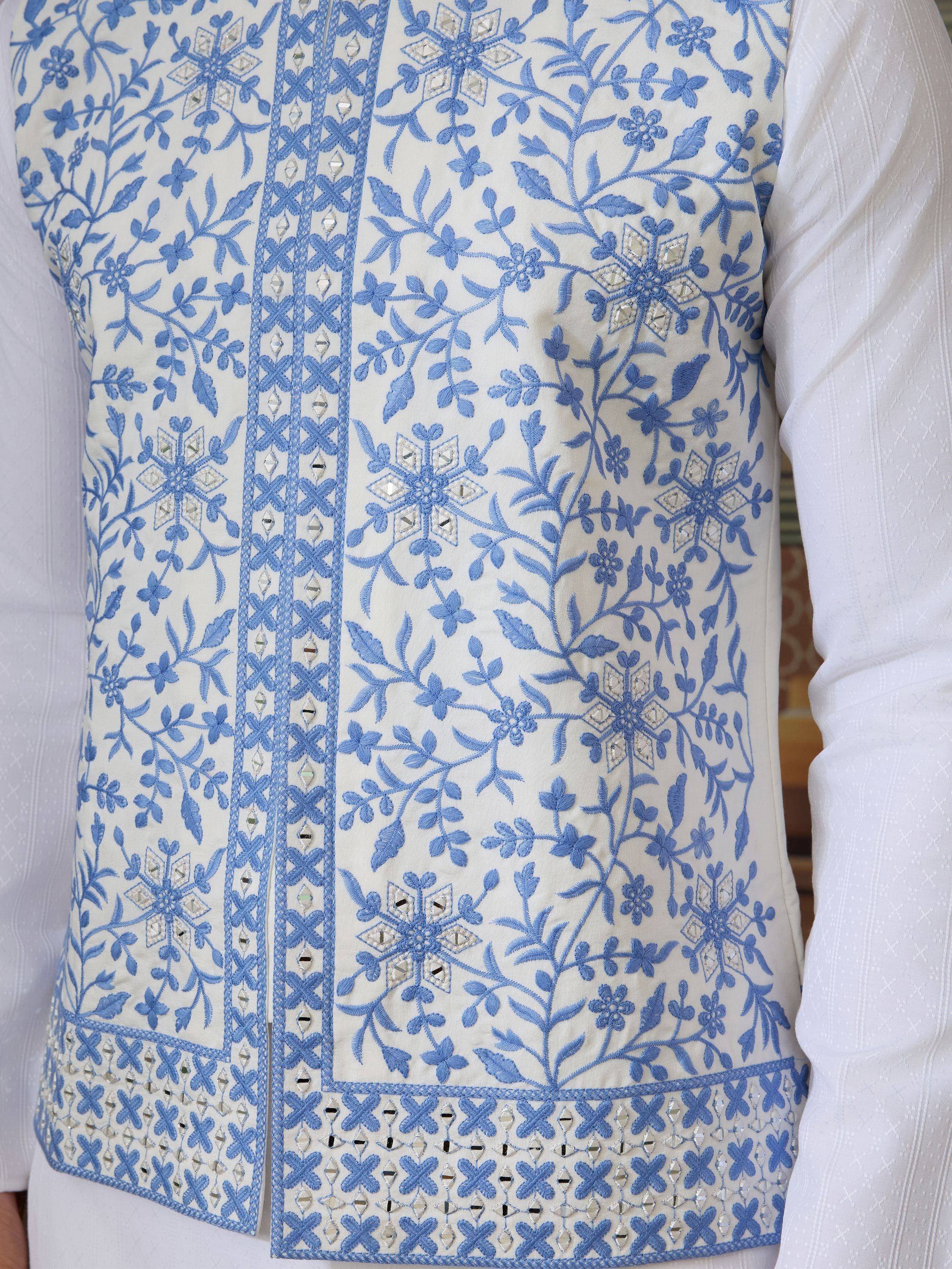 White ethnic vest with blue floral embroidery and mirror work, paired with white kurta for festive occasions.