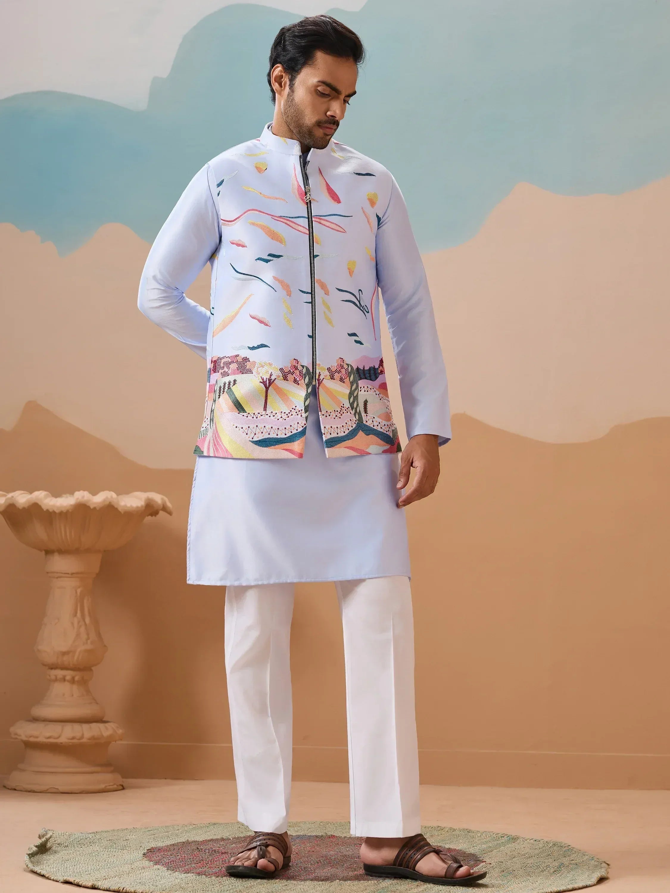 Man wearing light blue kurta with colorful printed Nehru jacket, white pants, and sandals for ethnic occasions