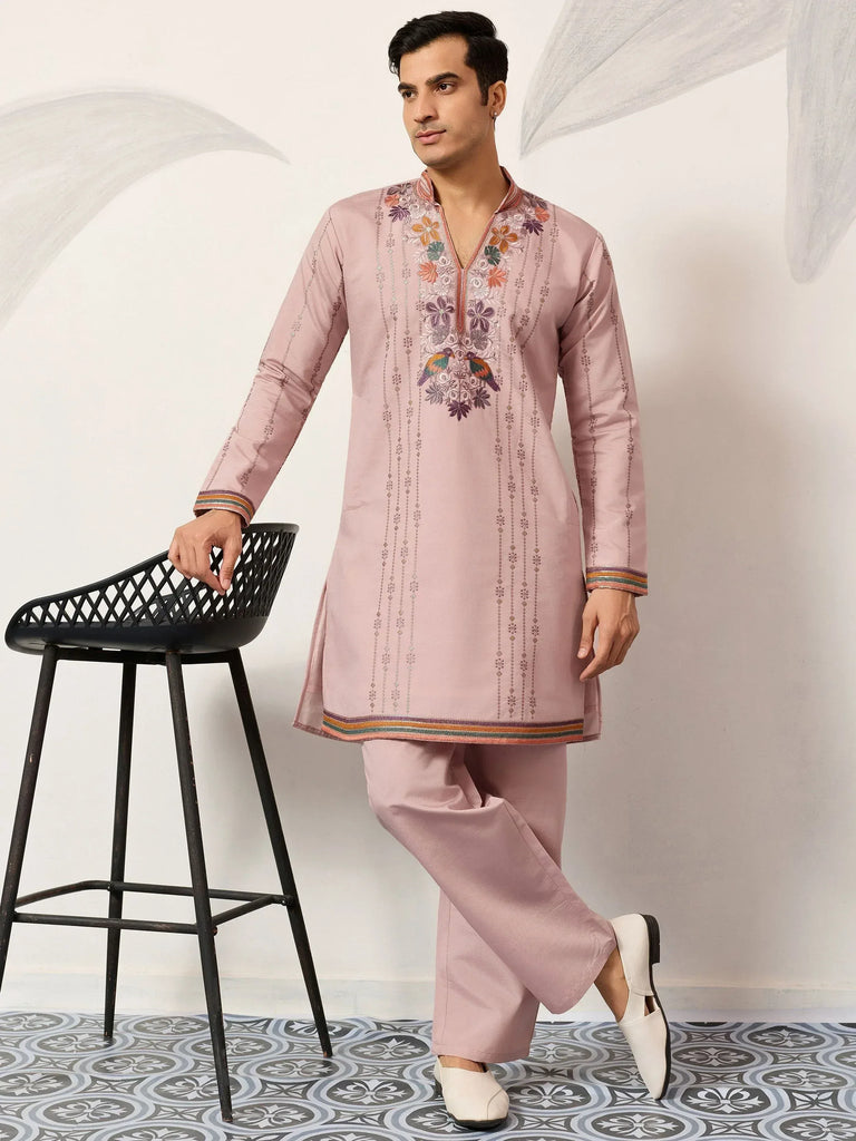 Men's pink embroidered kurta set with floral and bird motifs, paired with matching pants and white mojaris.