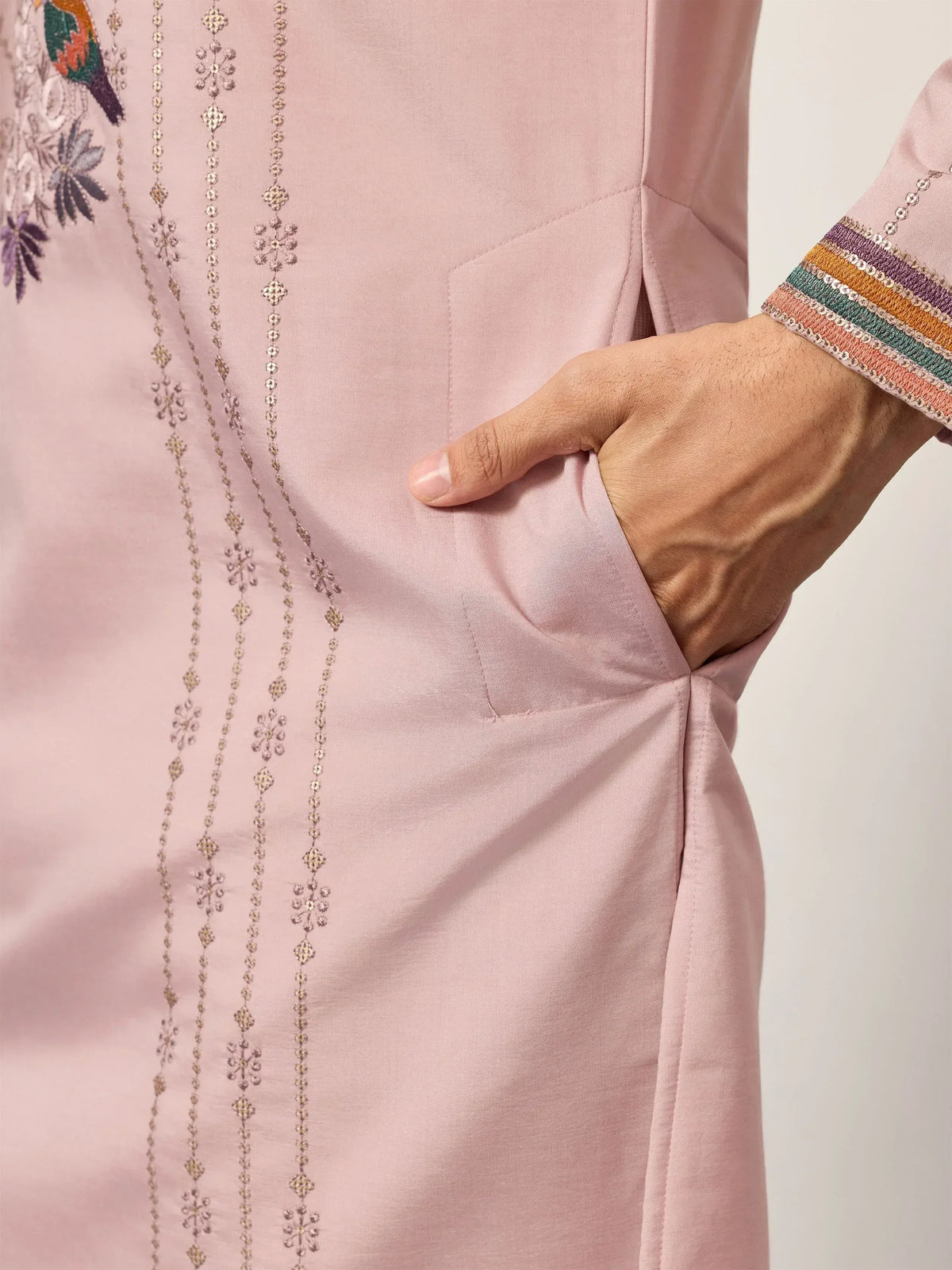 Pink ethnic kurta with floral embroidery, sequin detailing, and colorful striped cuffs, hand in pocket