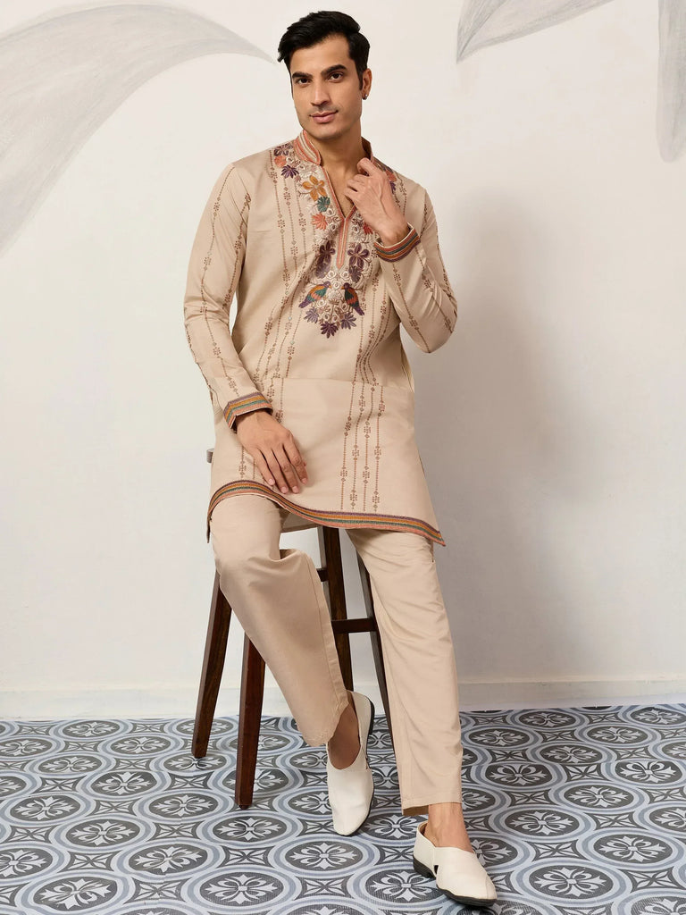Beige embroidered kurta set with floral and bird motifs, paired with matching pants and white mojari shoes.