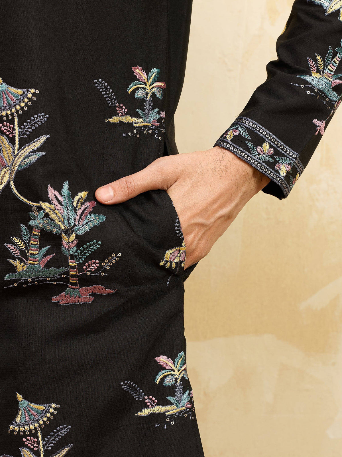 Close-up of a black men's ethnic kurta with colorful floral embroidery and a side pocket.