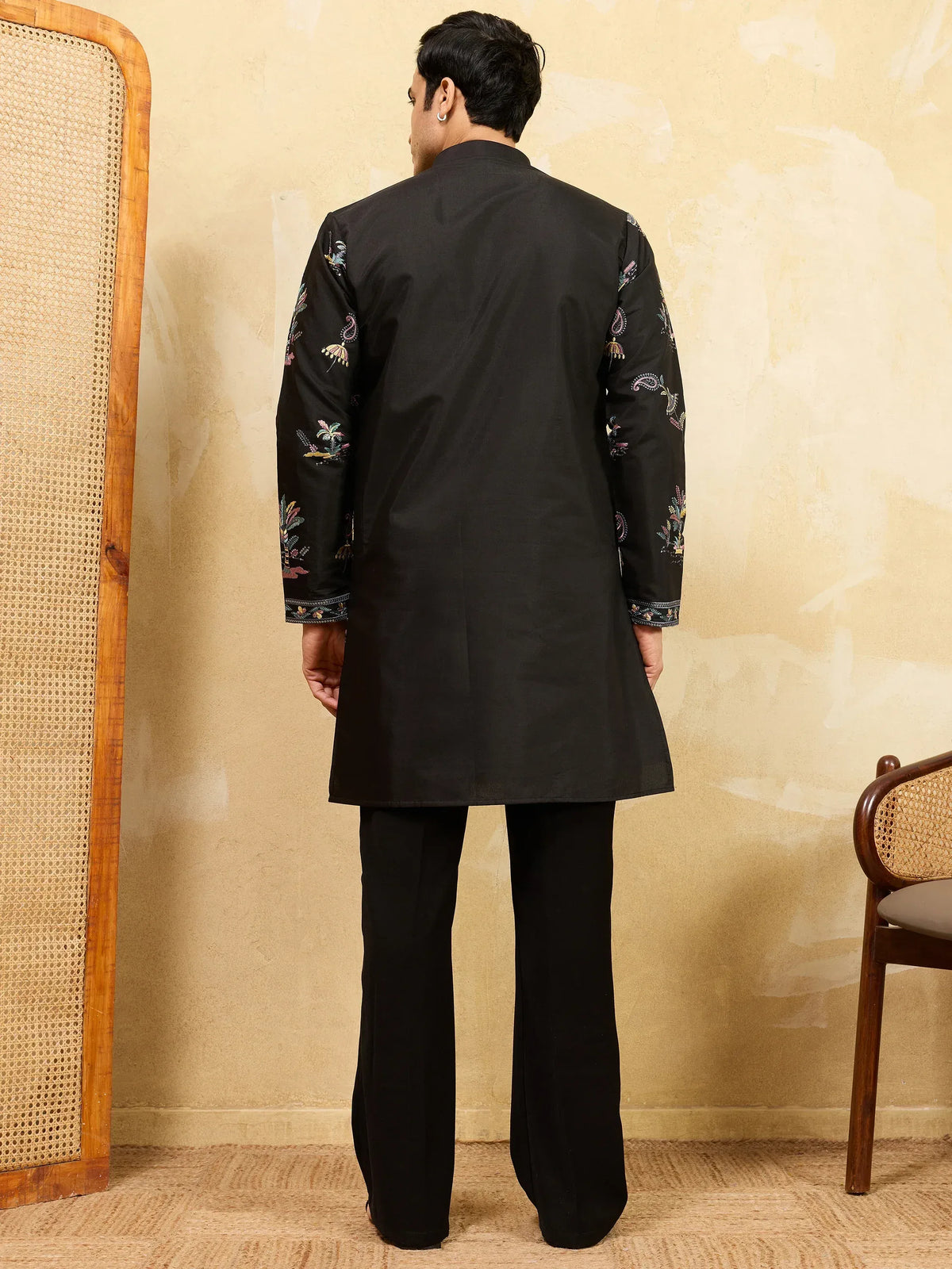 Back view of a man wearing a black embroidered ethnic sherwani with matching trousers
