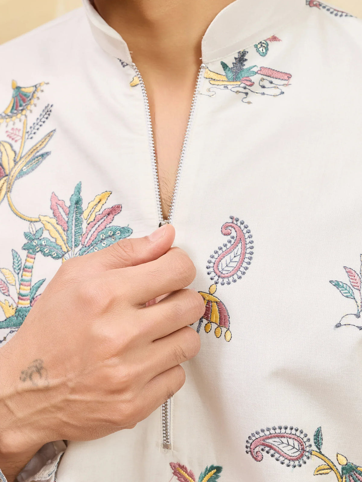 Close-up of a white men's ethnic garment with colorful floral embroidery and a zipper front.