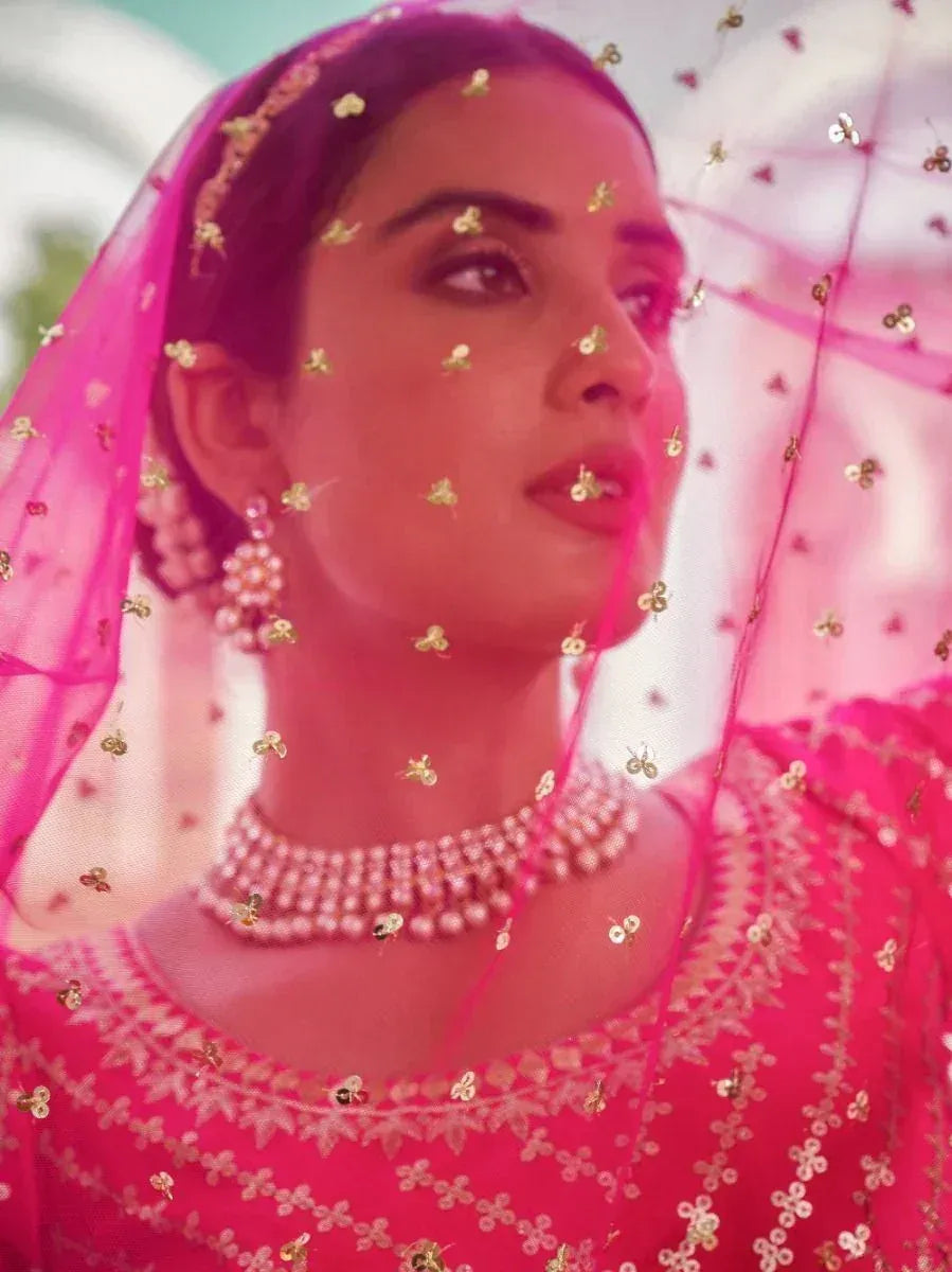 Pink embroidered lehenga choli with gold sequins, pearl jewelry, and sheer dupatta for Indian ethnic wear