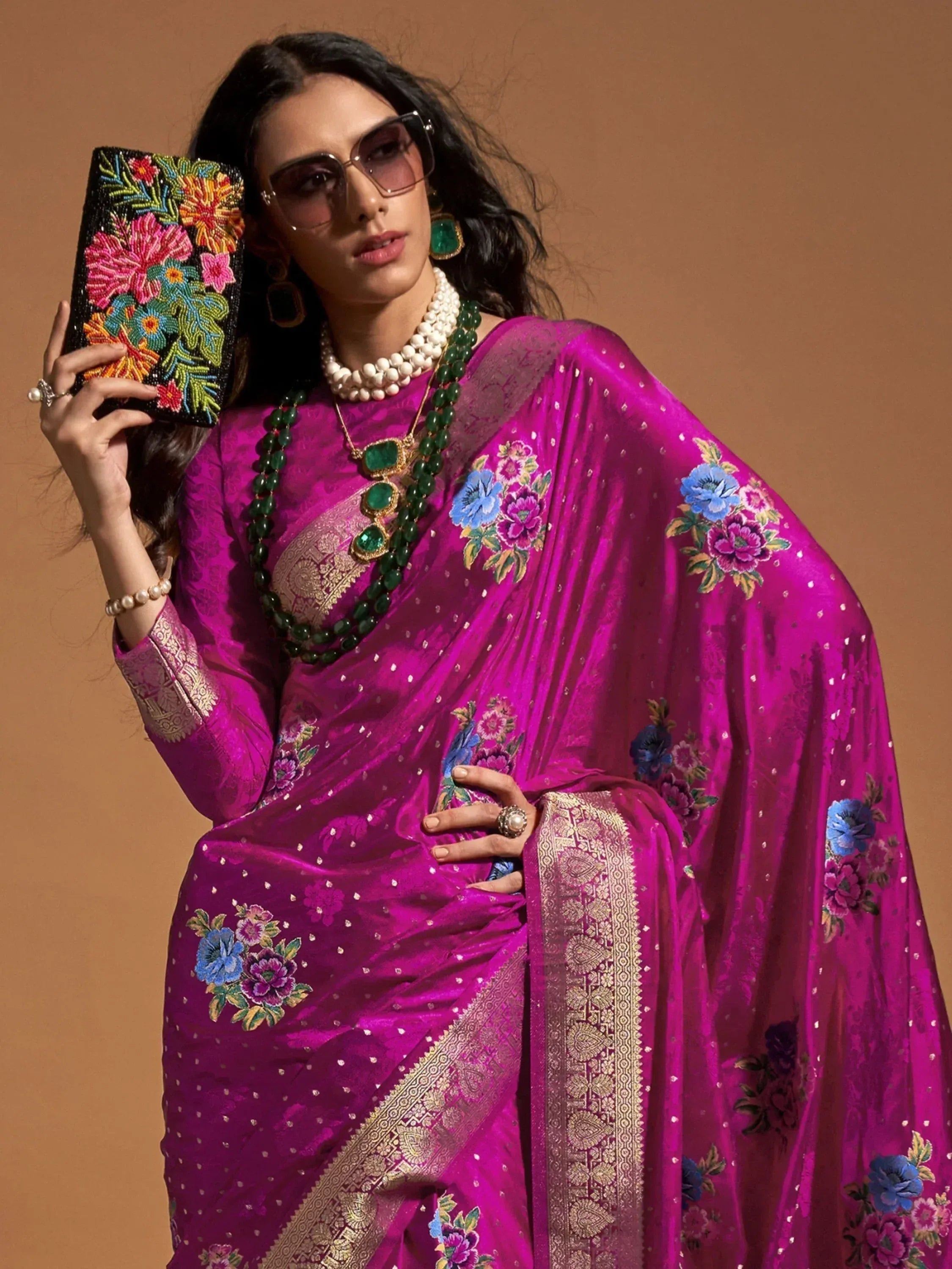 Vibrant magenta saree with floral embroidery and gold border, paired with statement jewelry and beaded clutch.