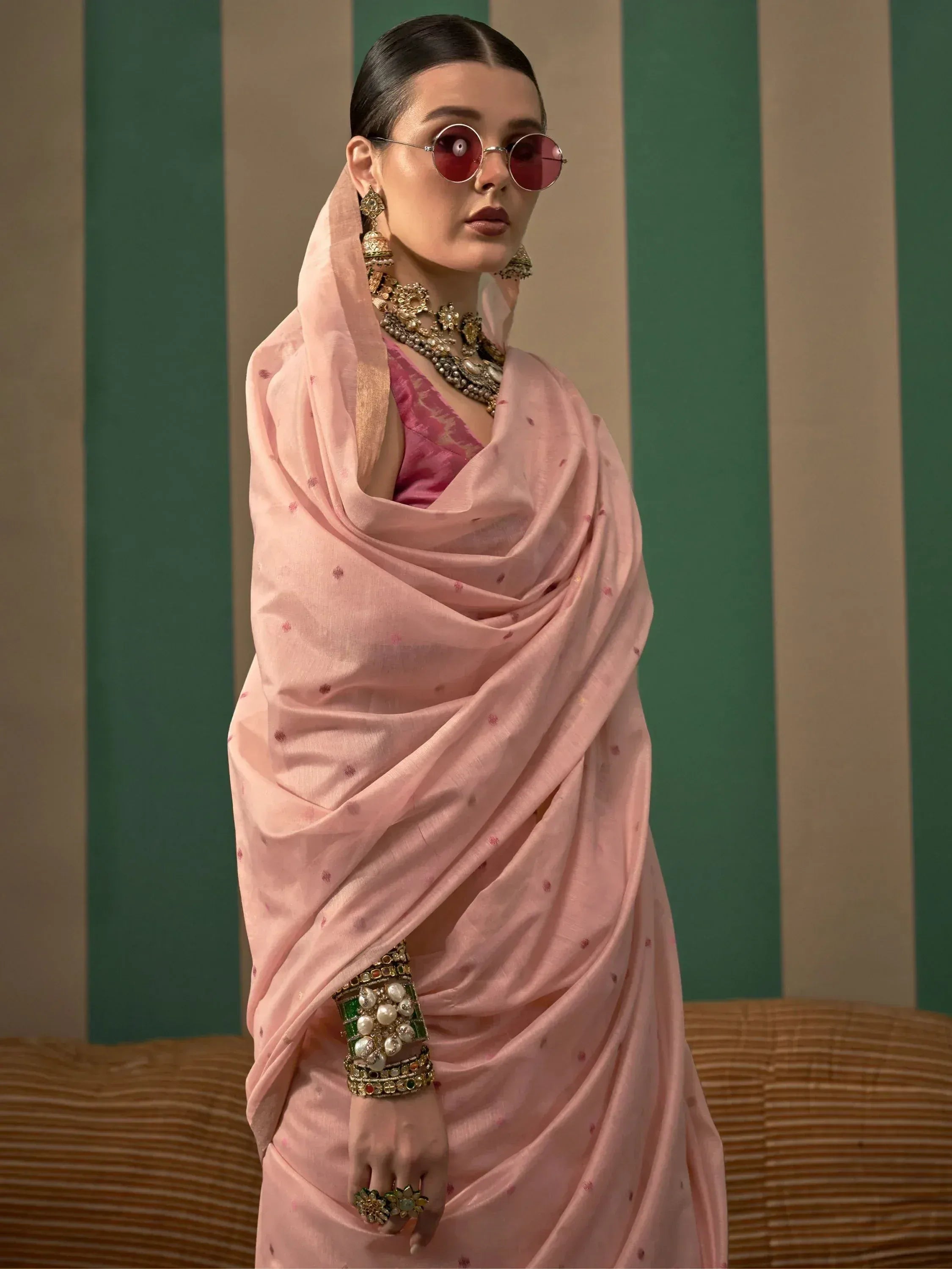 Woman in pink ethnic saree with gold jewelry and round sunglasses, styled for Indian fashion