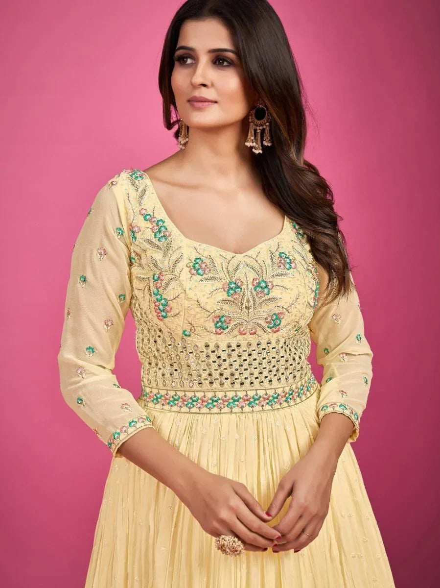 Woman in a yellow embroidered ethnic gown with mirror work, set against pink background