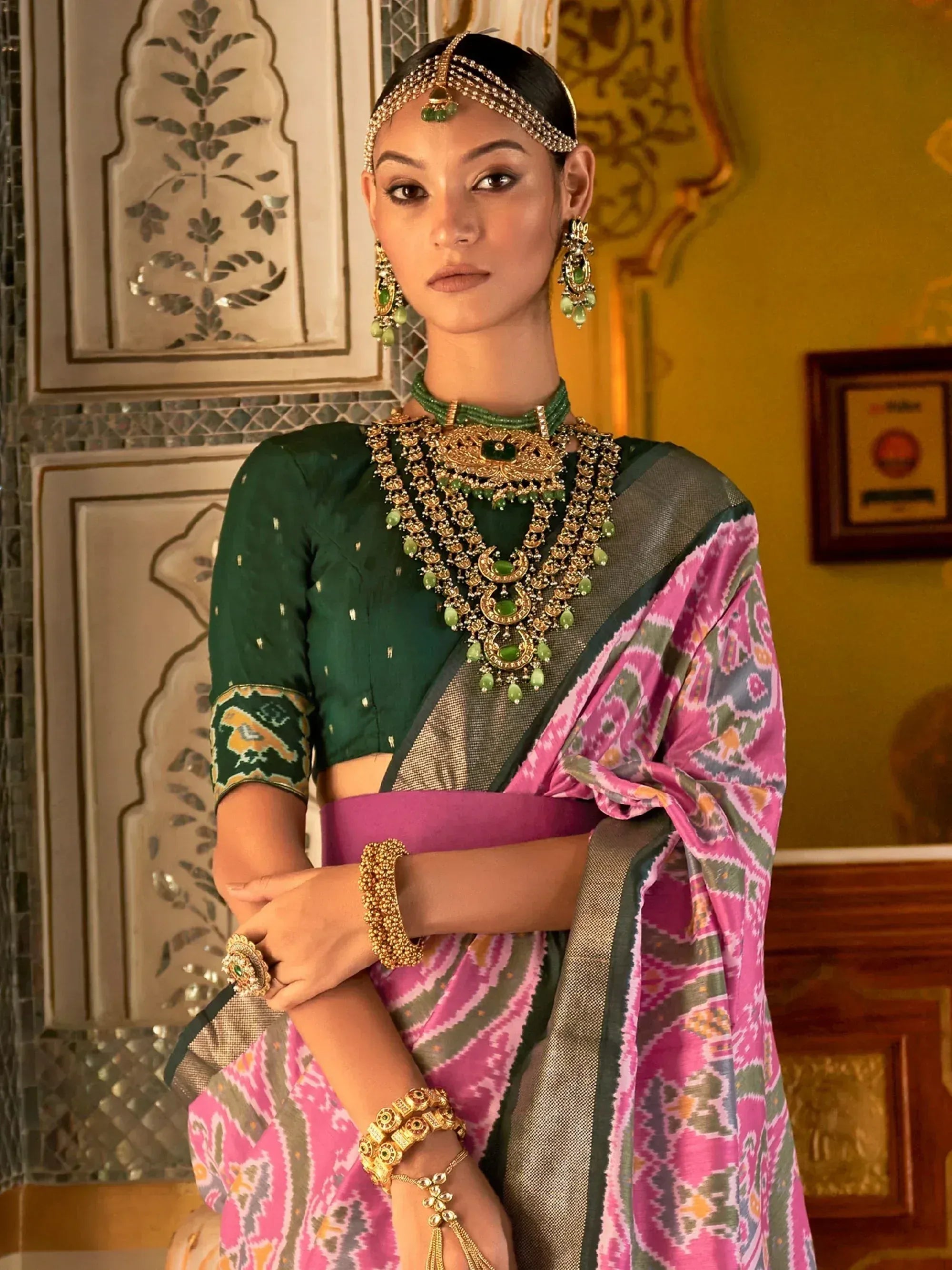 Elegant woman in green blouse and pink ikat saree with traditional gold jewelry, perfect for Indian ethnic wear occasions.