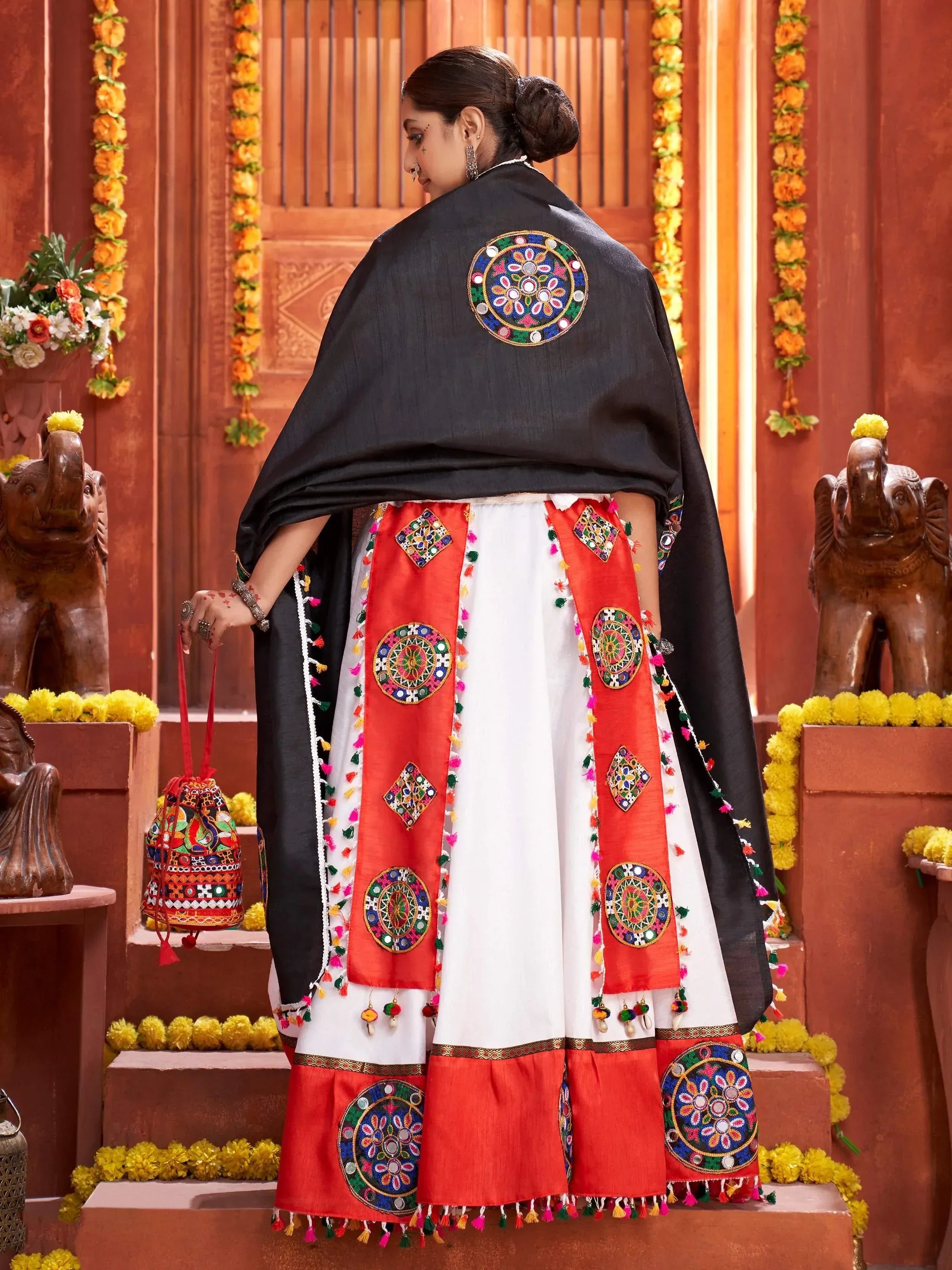 Woman in traditional Indian ethnic wear with mirror work, embroidered skirt, and black dupatta, festive setting