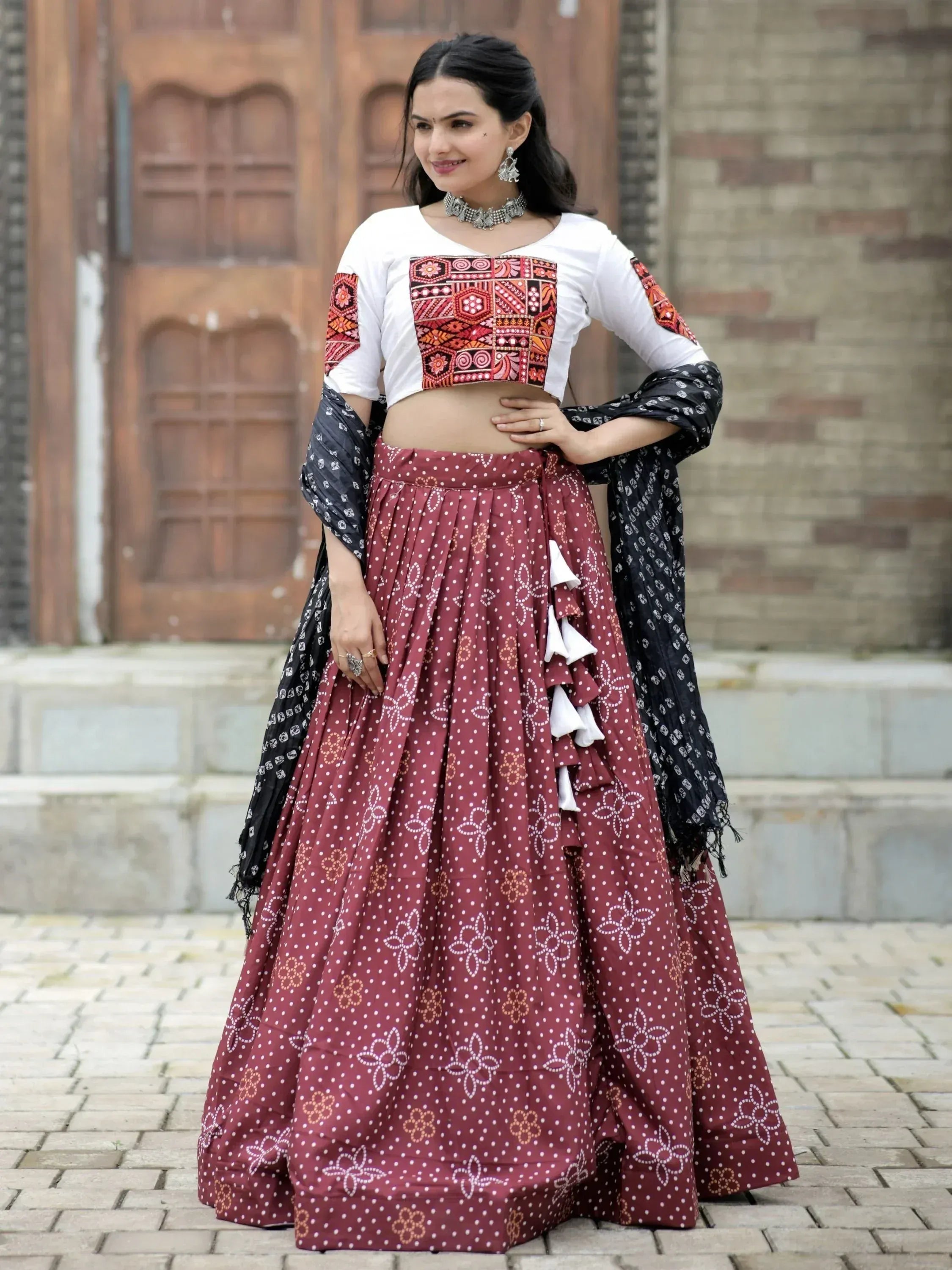 Woman in maroon printed lehenga with embroidered white crop top and black dupatta, ethnic Indian wear