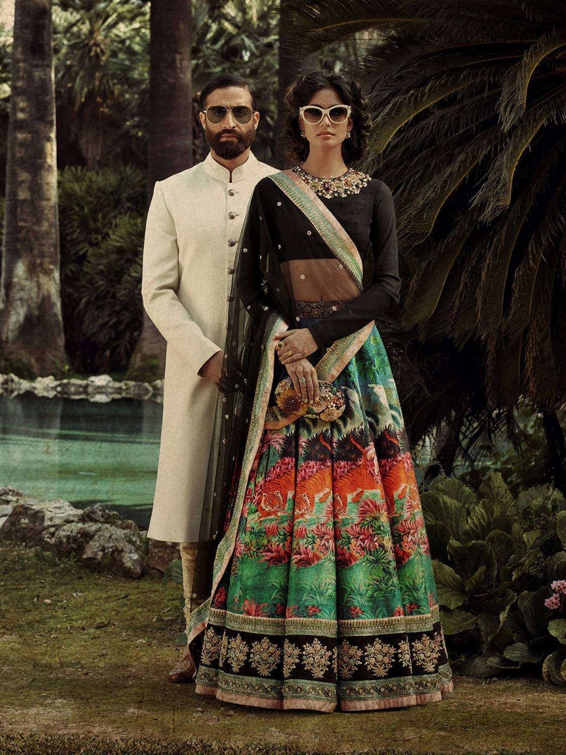 Woman in printed lehenga choli with man in cream sherwani, tropical garden setting