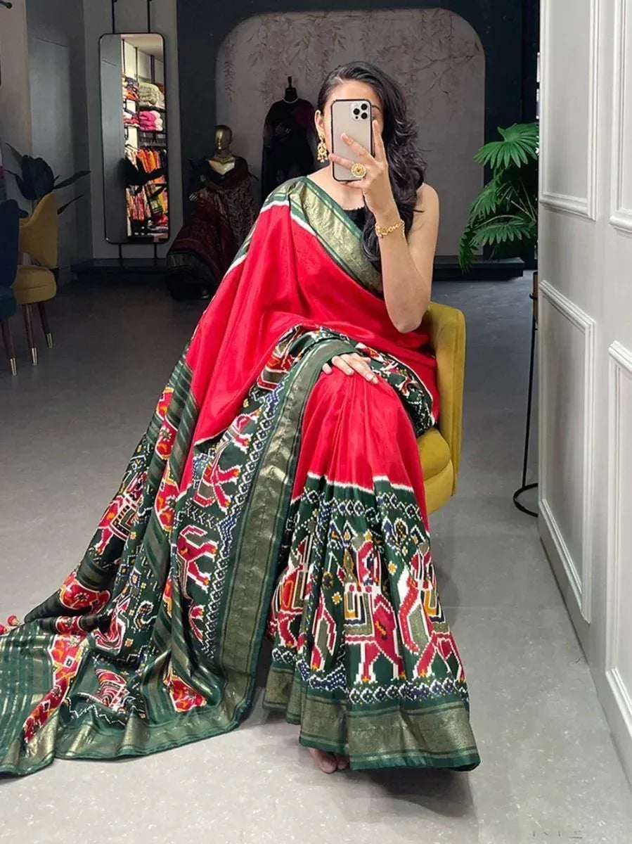 Woman in red and green printed saree with ethnic motifs, seated in boutique setting