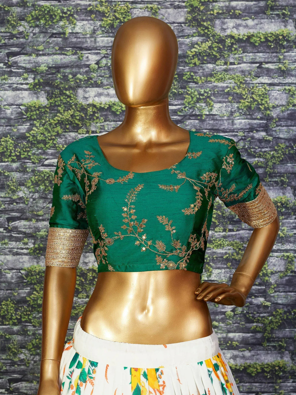 Emerald green embroidered blouse with gold floral work, paired with floral lehenga, displayed on mannequin