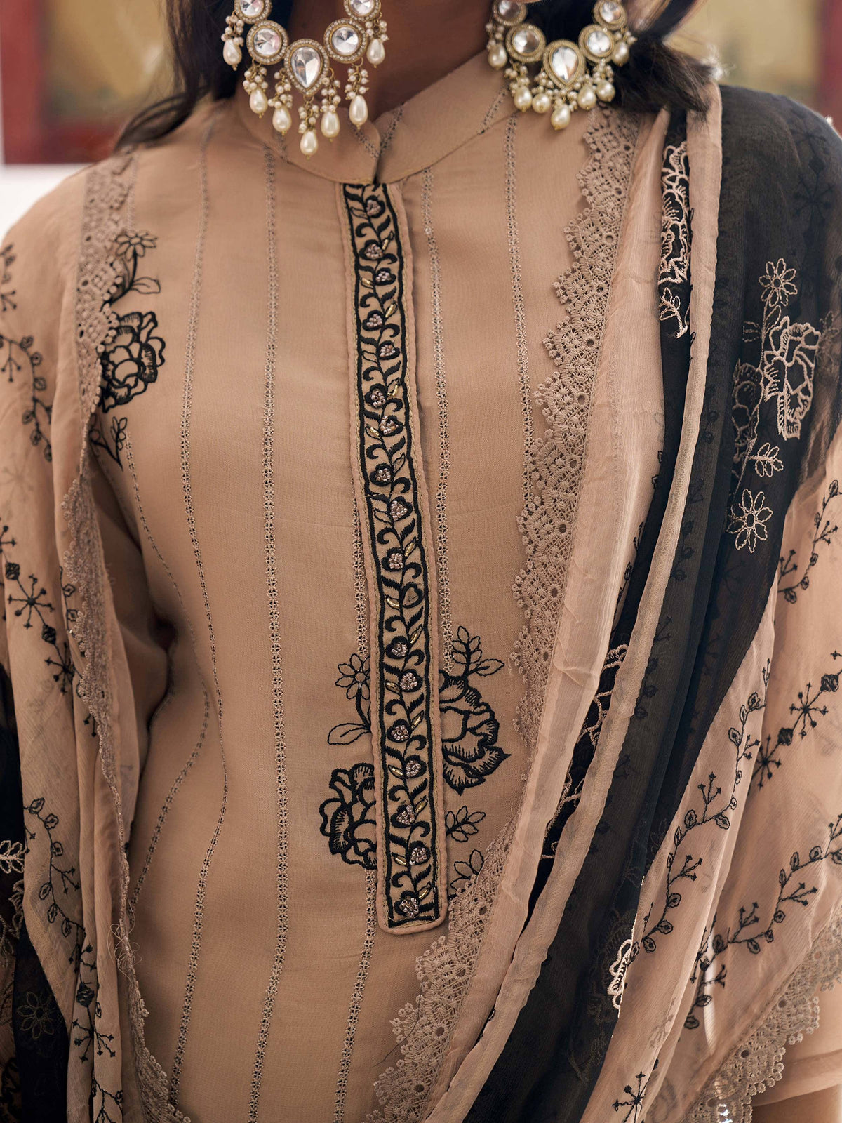 Elegant beige salwar kameez with black floral embroidery, lace detailing, and statement jewelry