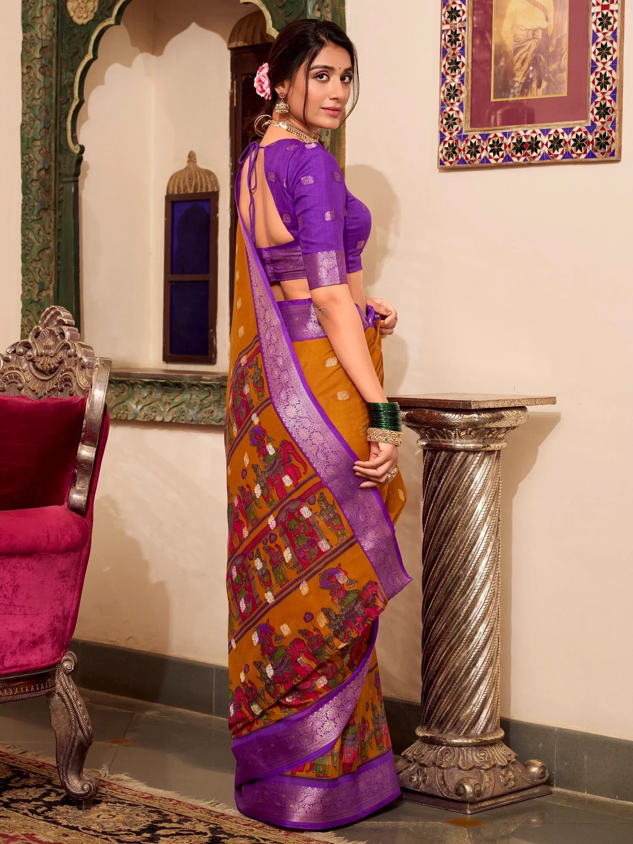 Woman in purple and mustard Indian saree with temple print, backless blouse, ethnic jewelry, traditional setting