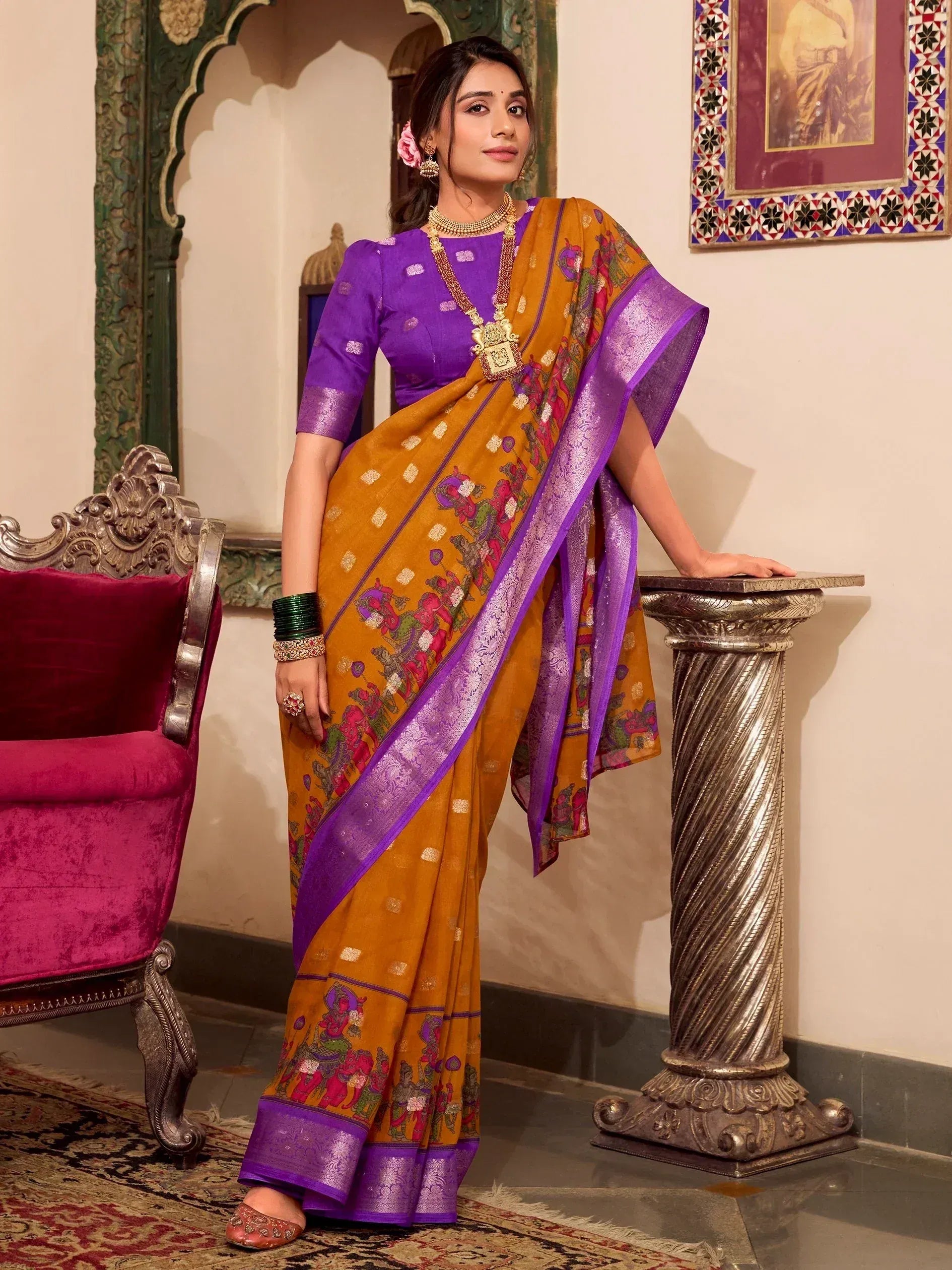 Woman in mustard and purple ethnic saree with temple print, paired with designer blouse and gold jewelry