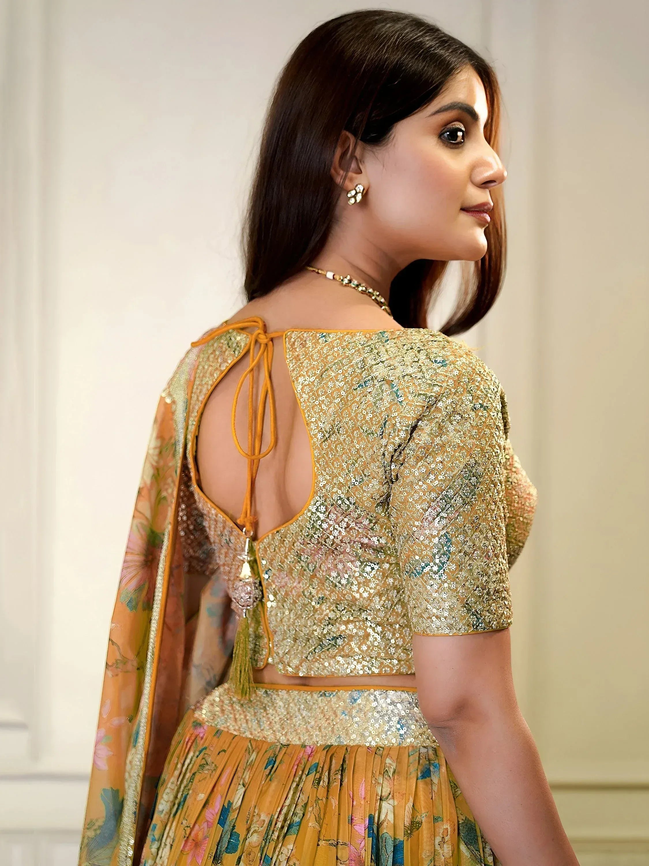 Woman in gold sequin lehenga choli with floral print and open back design, perfect for Indian ethnic wear.