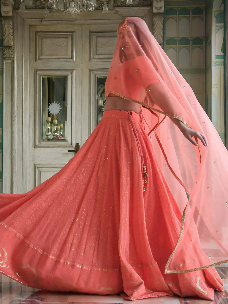 Person wearing a traditional pink outfit with a long veil in an elegant interior setting.