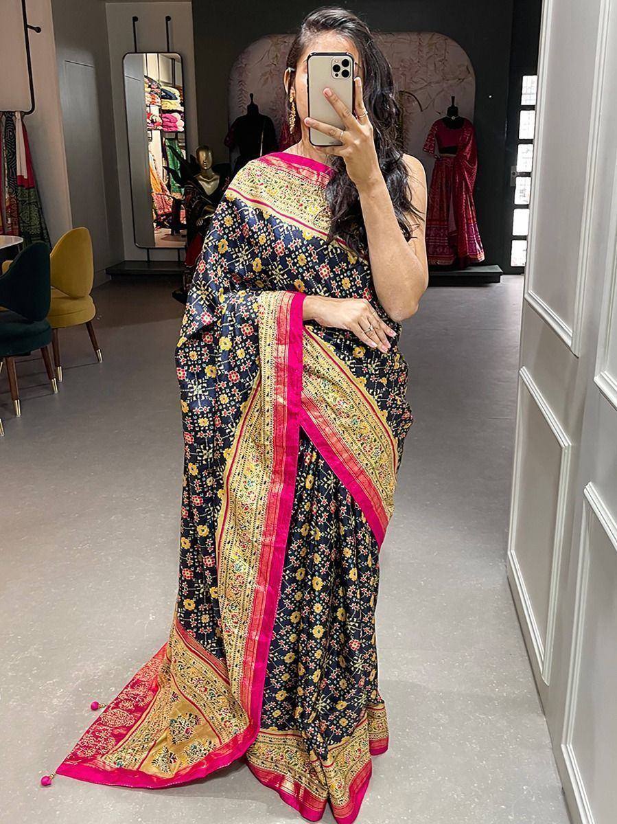 Woman in black floral saree with pink and gold border, taking mirror selfie in boutique