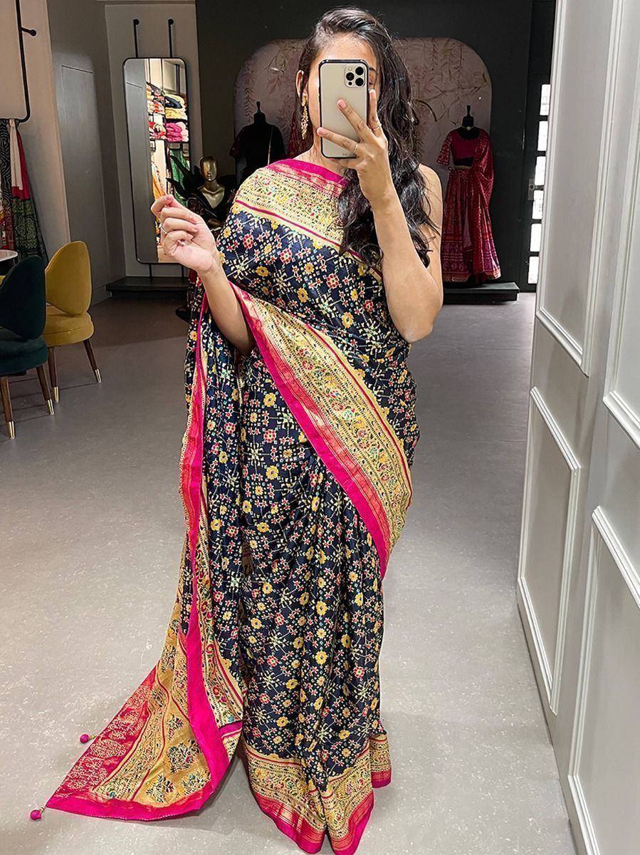 Woman wearing black floral saree with pink and gold border, taking mirror selfie in boutique