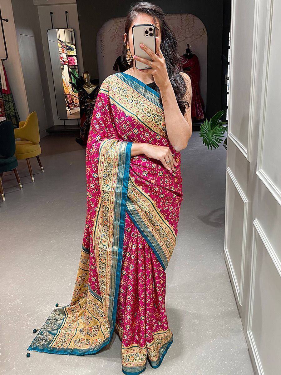 Woman in vibrant pink floral saree with gold and blue border, taking mirror selfie in boutique