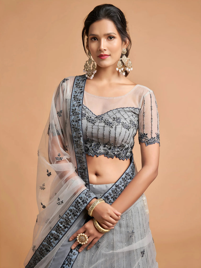 Woman wearing a grey designer lehenga choli with intricate embroidery and a matching dupatta.