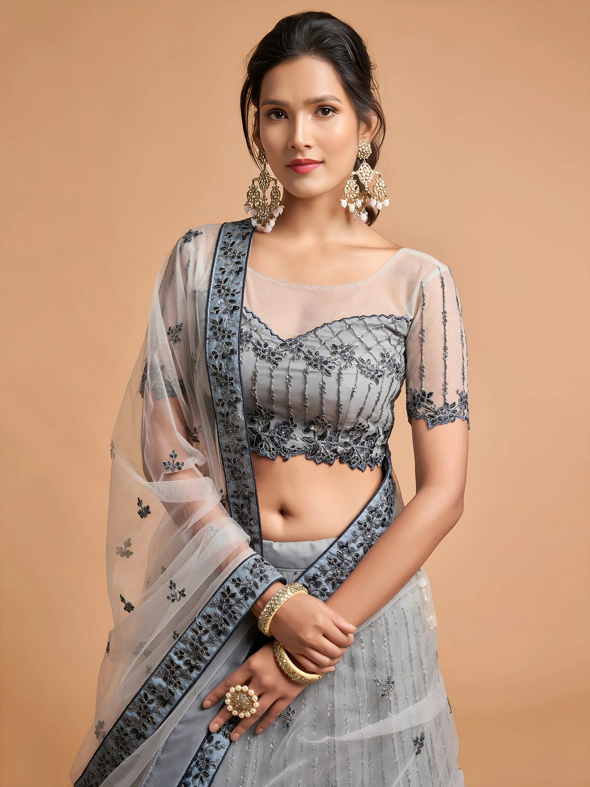 Woman wearing a grey designer lehenga choli with intricate embroidery and a matching dupatta.