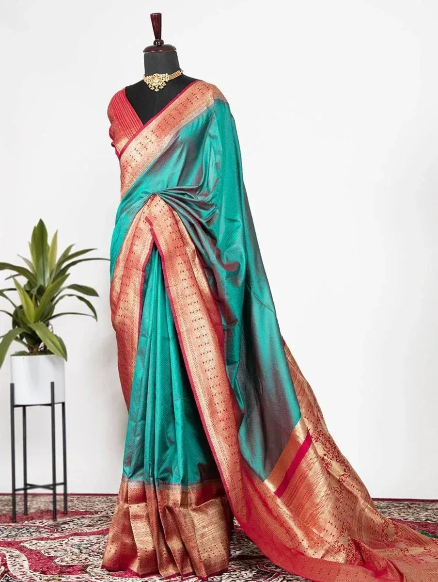 Teal and red designer saree with gold border, displayed on mannequin with traditional jewelry